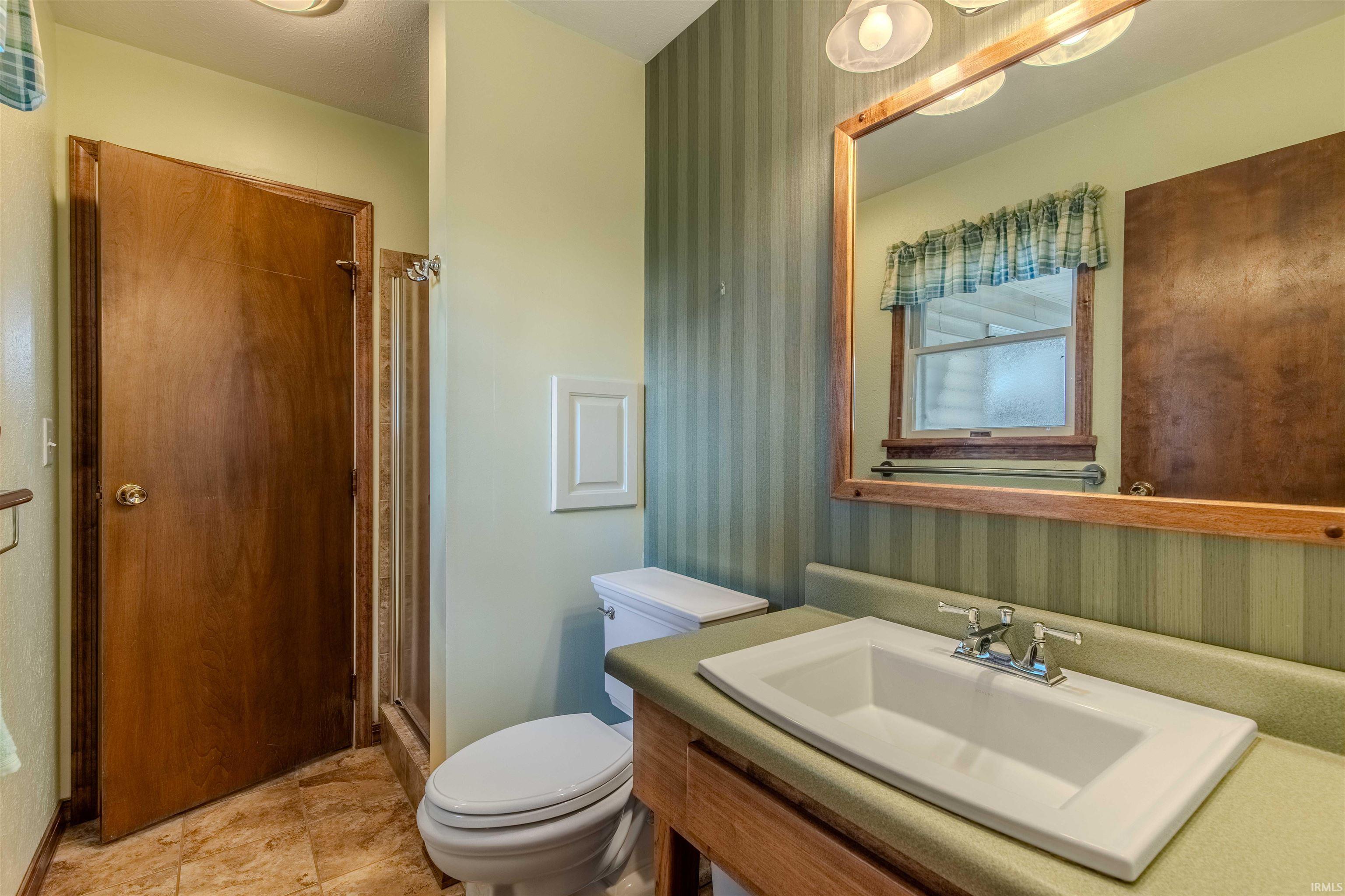 Full bathroom with wallpapered walls, vanity, and a shower stall