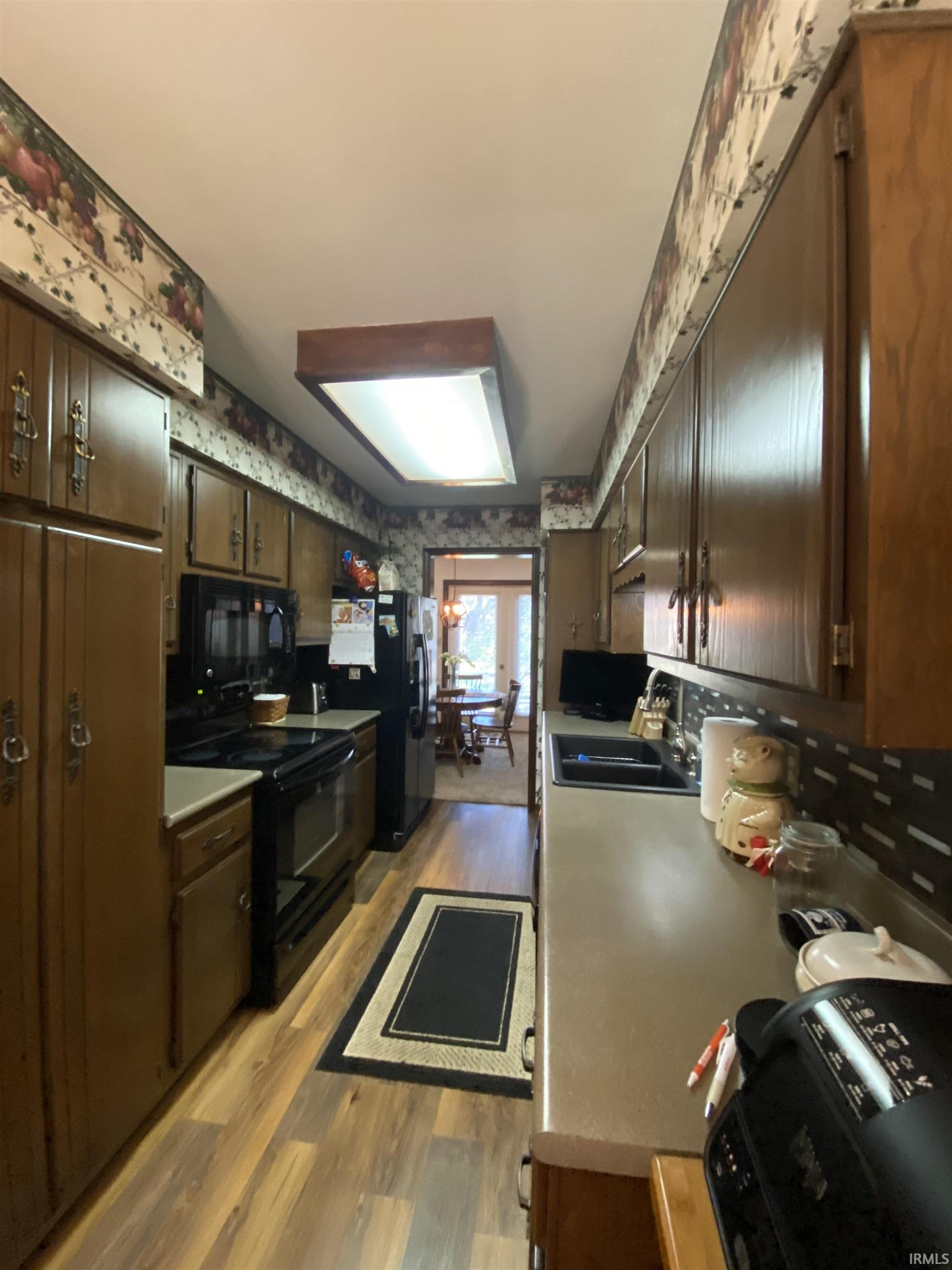 Kitchen featuring wallpapered walls, black appliances, light wood-style floors, light countertops, and dark wood finish cabinetry