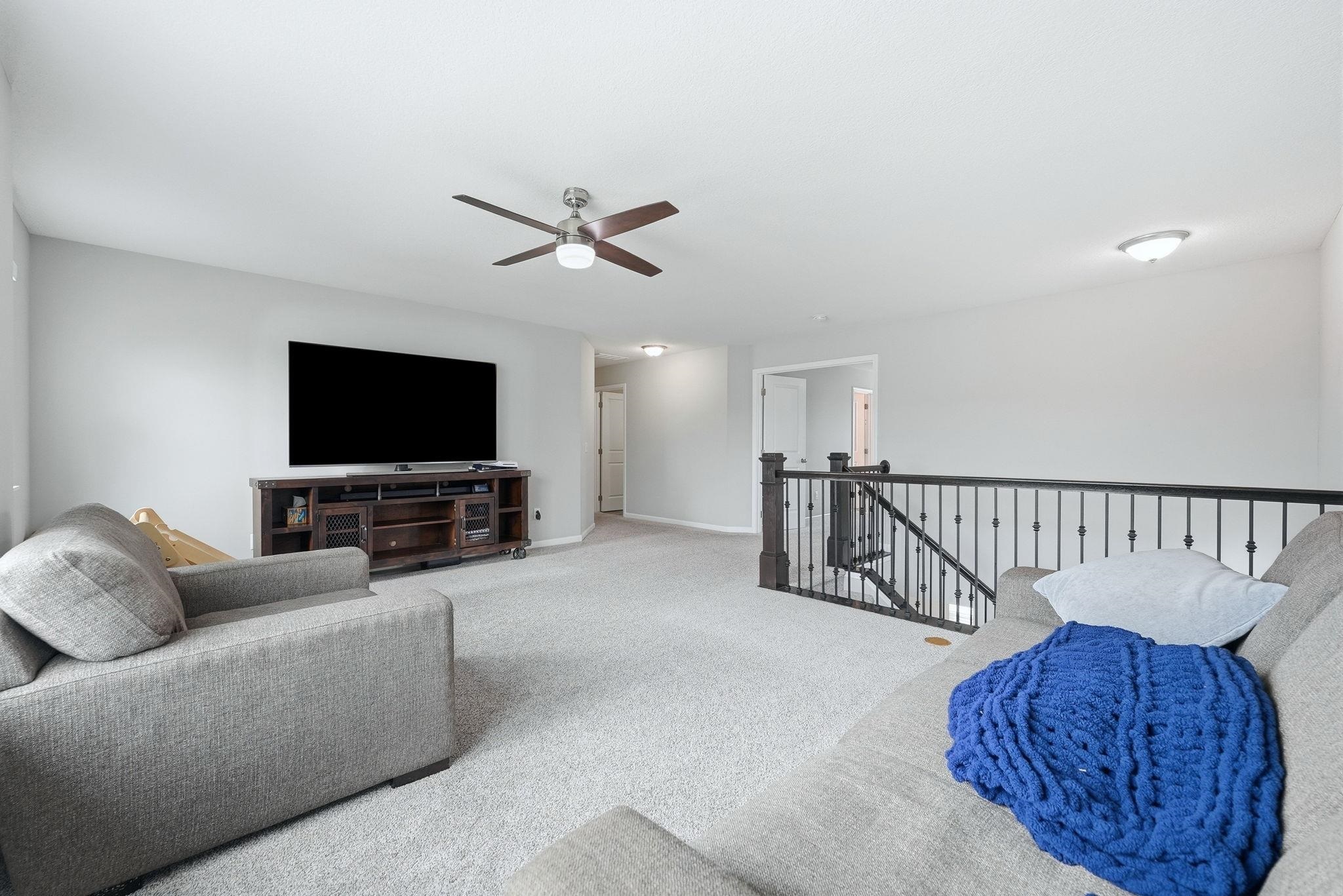 Carpeted living area featuring ceiling fan and baseboards