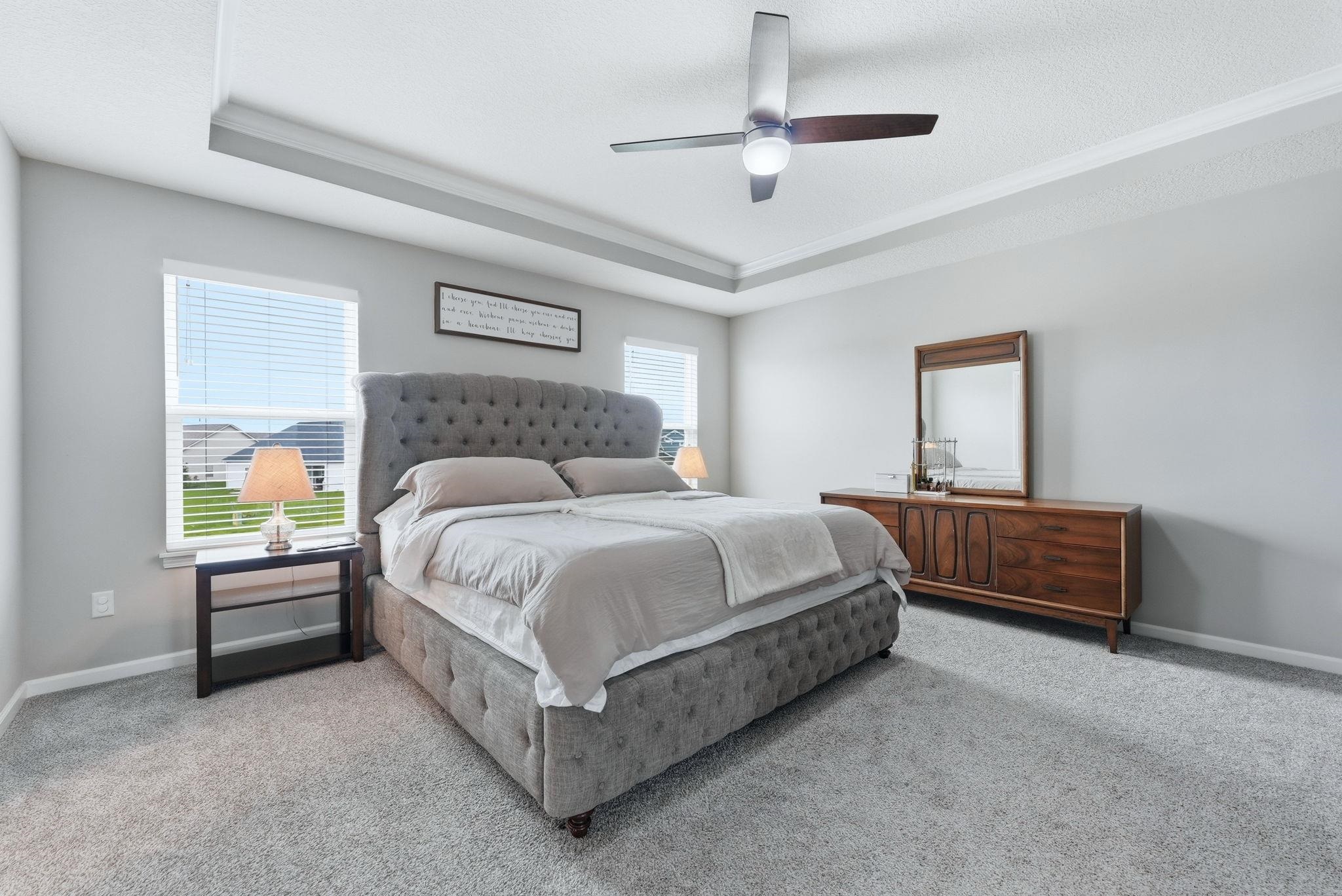 Bedroom with a ceiling fan, light colored carpet, a tray ceiling, and crown molding