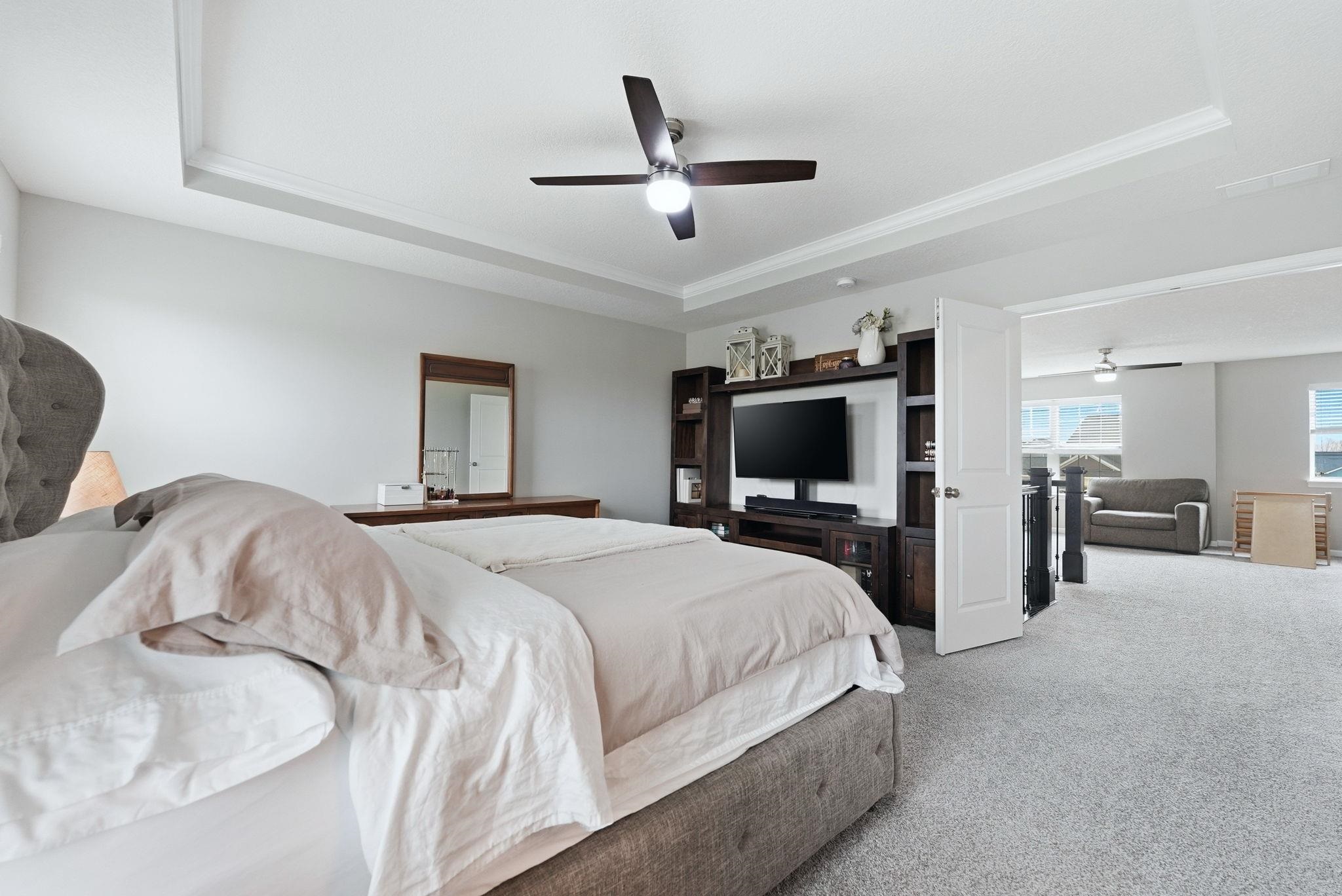 Bedroom with carpet flooring, a raised ceiling, crown molding, and ceiling fan