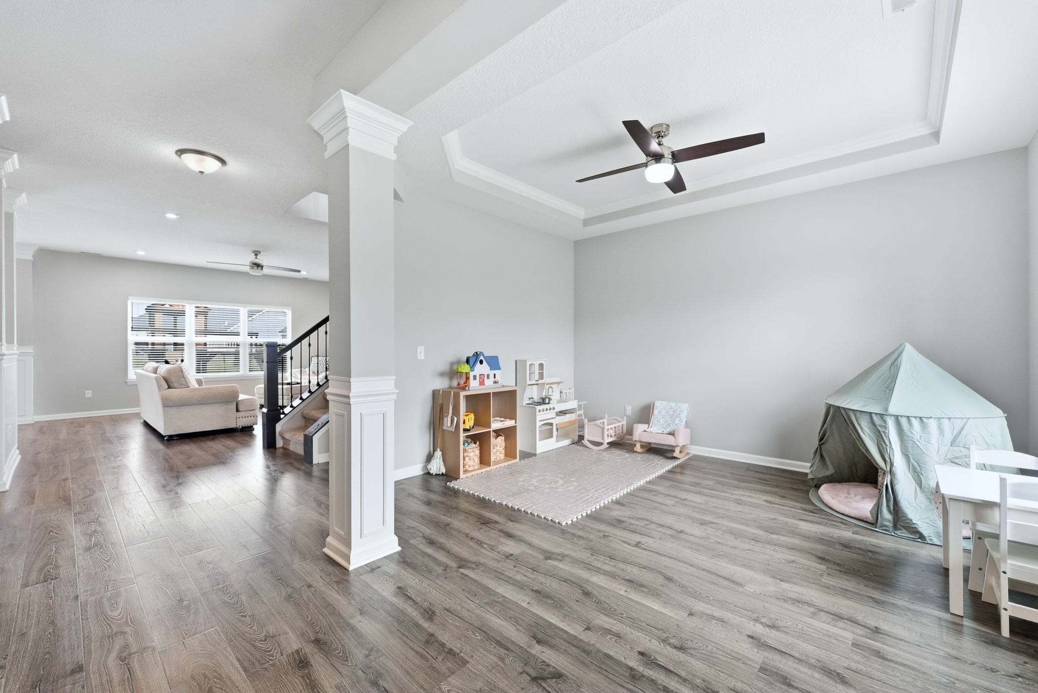 Recreation room with ceiling fan, dark wood finished floors, decorative columns, and a raised ceiling