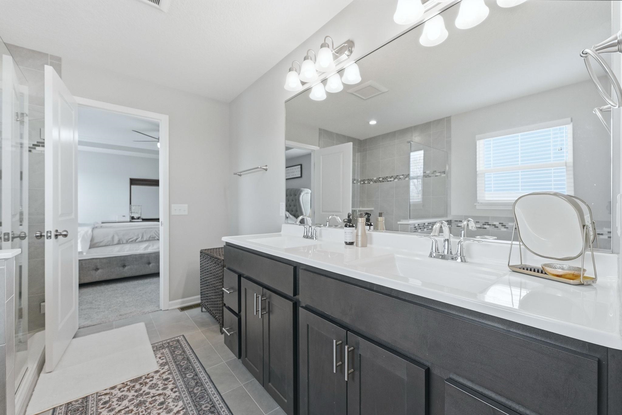 Full bathroom with ensuite bath, double vanity, light tile patterned flooring, and tiled shower