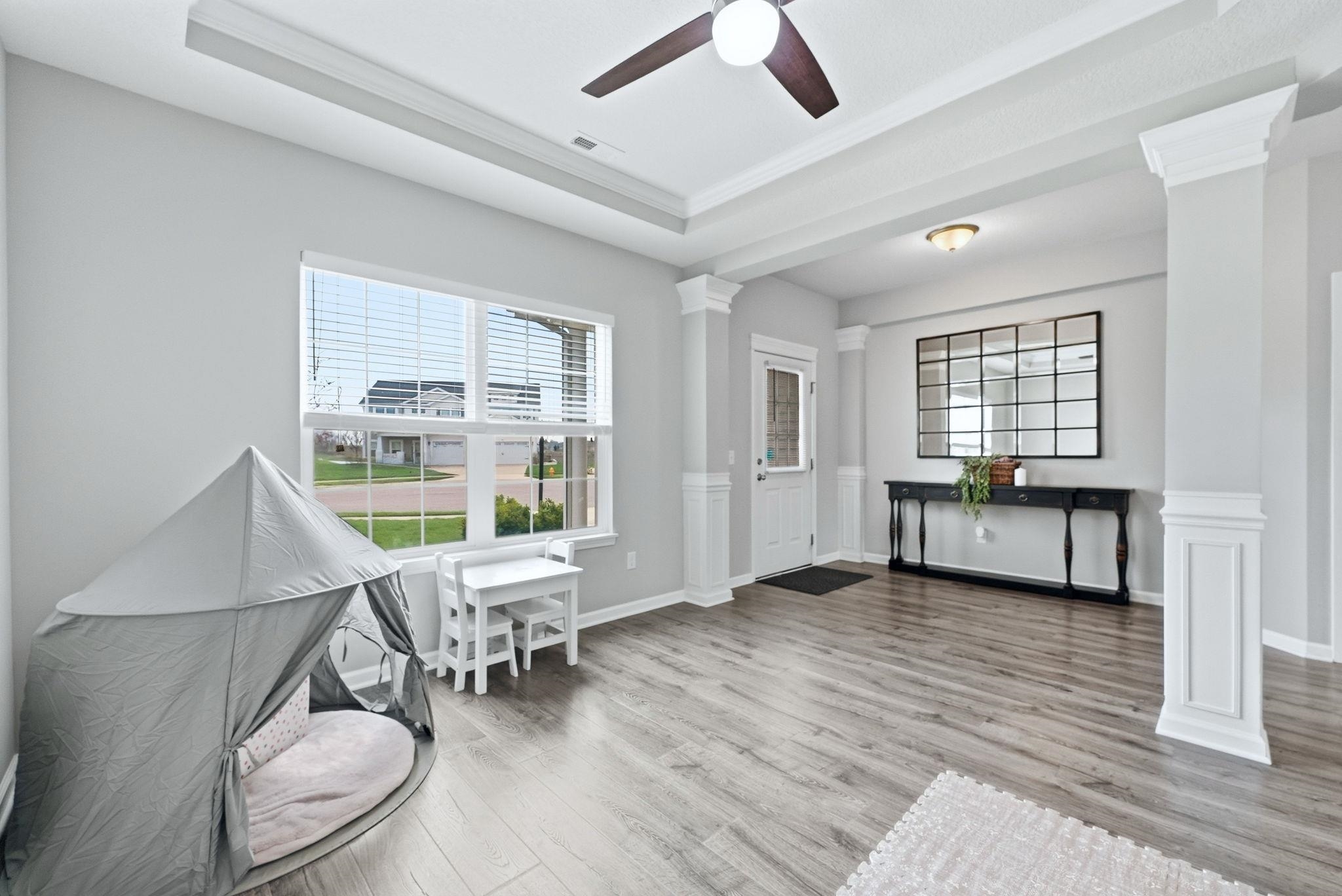 Living area with decorative columns, a raised ceiling, plenty of natural light, light wood-type flooring, and ceiling fan