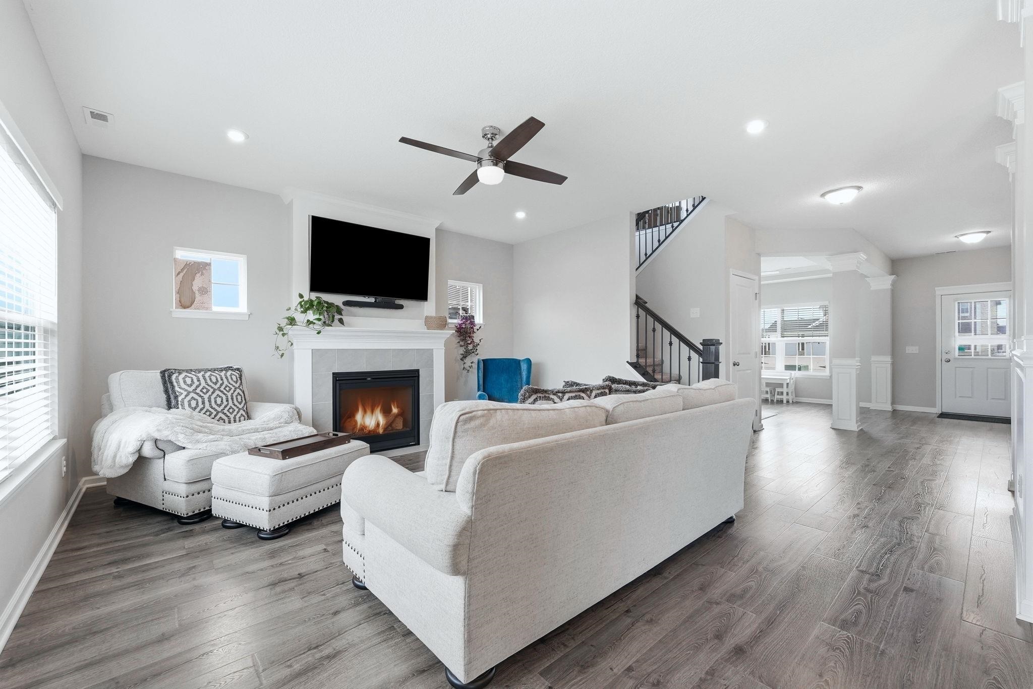 Living area featuring wood finished floors, a fireplace, ceiling fan, and decorative columns