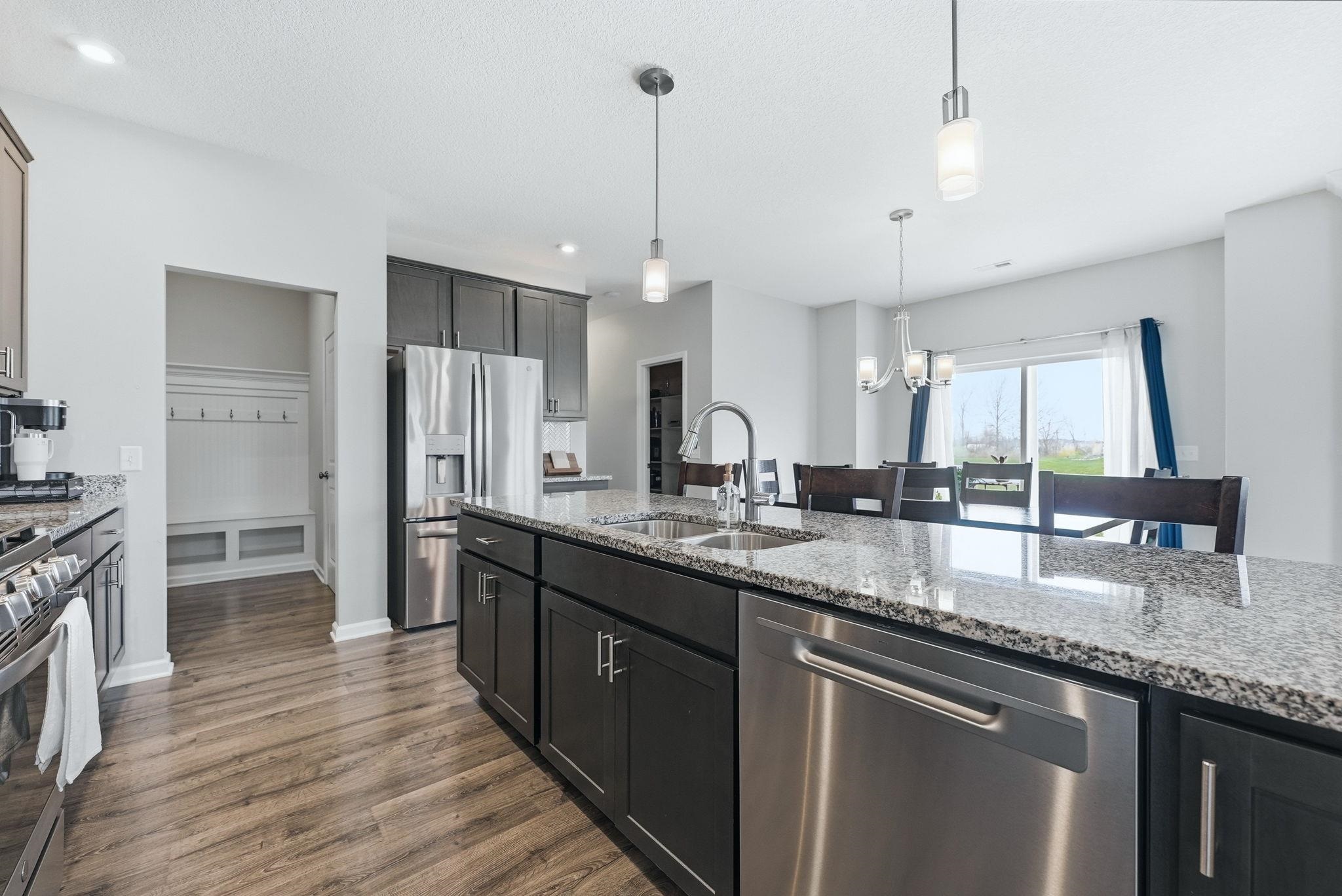 Kitchen featuring hanging lights, stainless steel appliances, light stone counters, dark wood-type flooring, and a textured ceiling