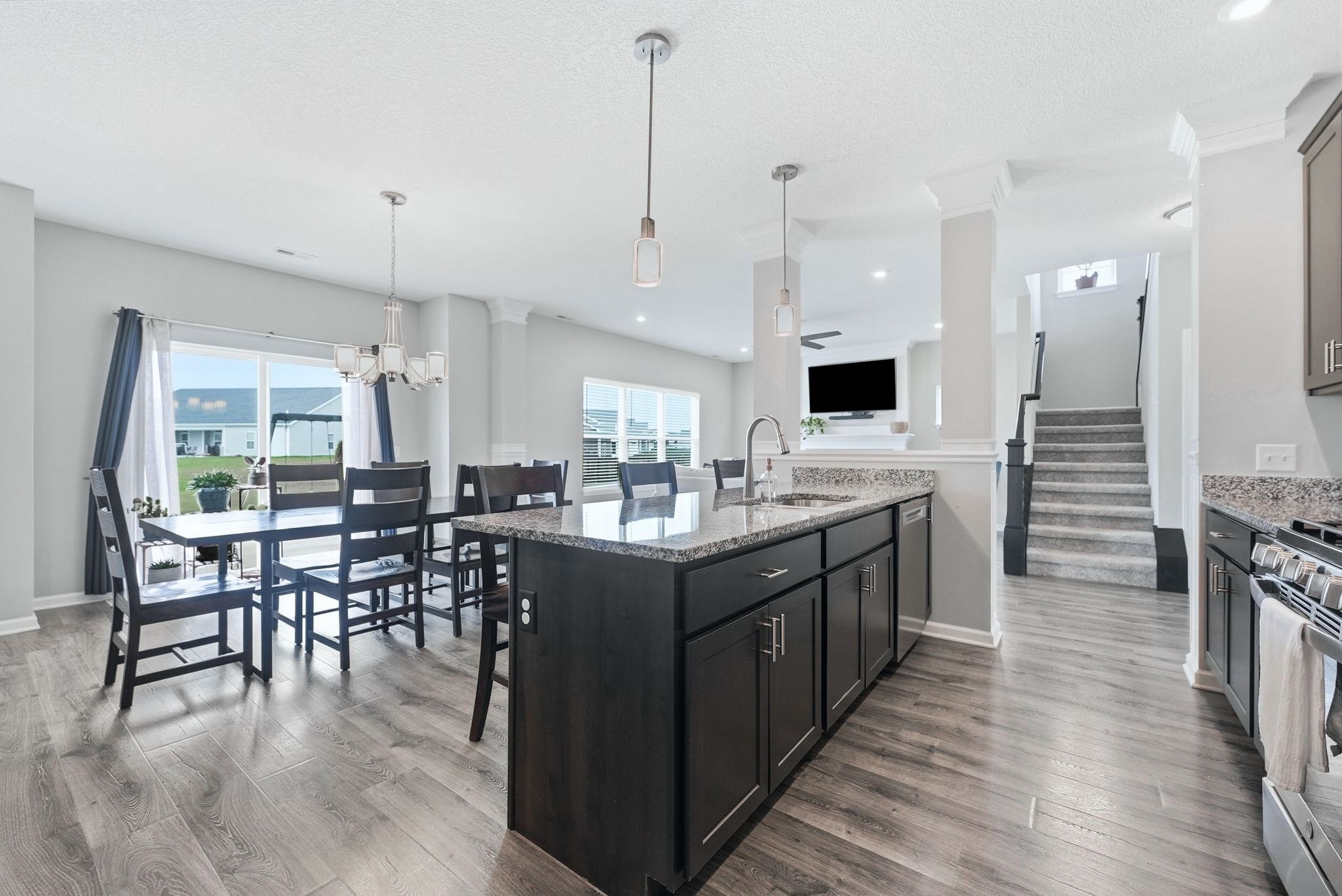 Kitchen with light stone countertops, a breakfast bar, dark wood-style floors, stainless steel appliances, and suspended lighting