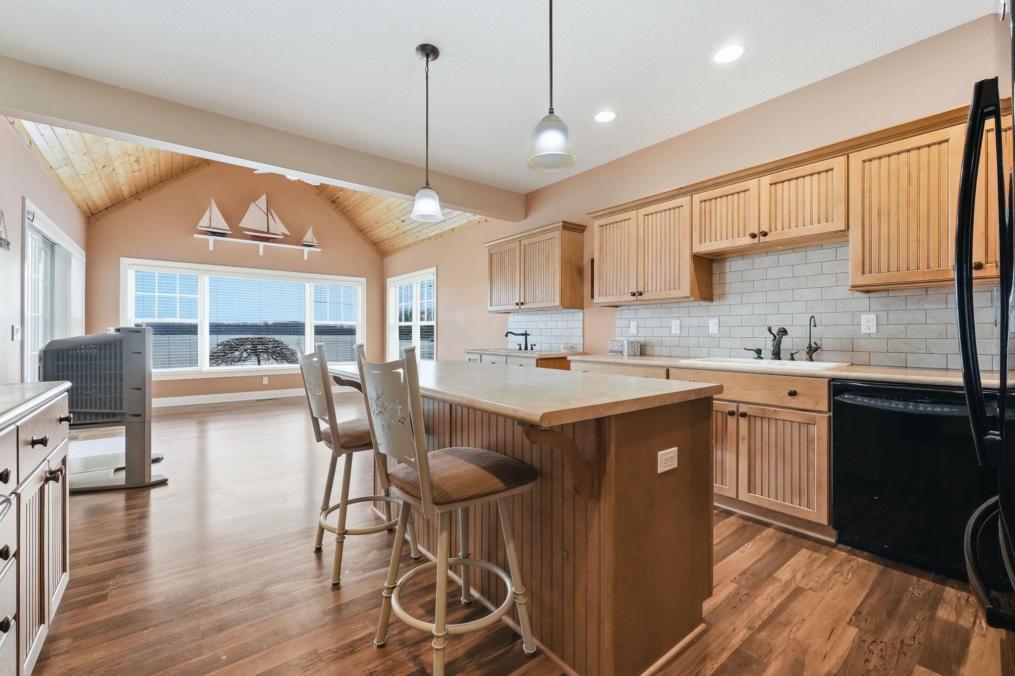 Kitchen with light wood finish cabinetry, dark wood-style floors, black appliances, a kitchen island, and a kitchen bar
