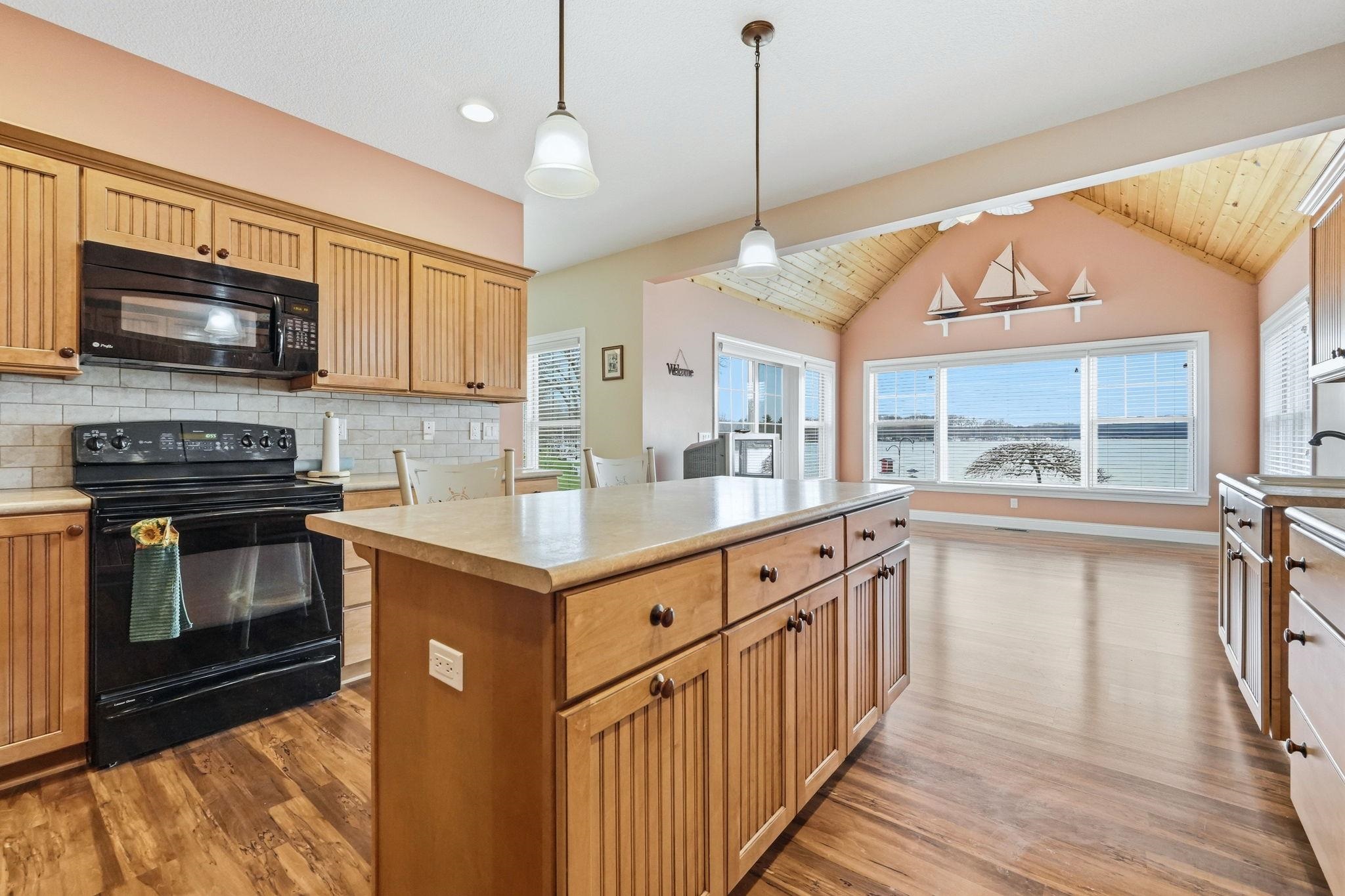 Kitchen featuring black appliances, light countertops, dark wood finished floors, hanging light fixtures, and a center island