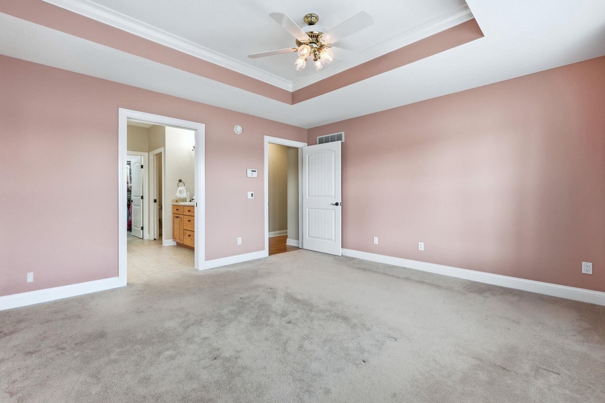 Unfurnished bedroom featuring ensuite bath, light carpet, crown molding, ceiling fan, and a tray ceiling