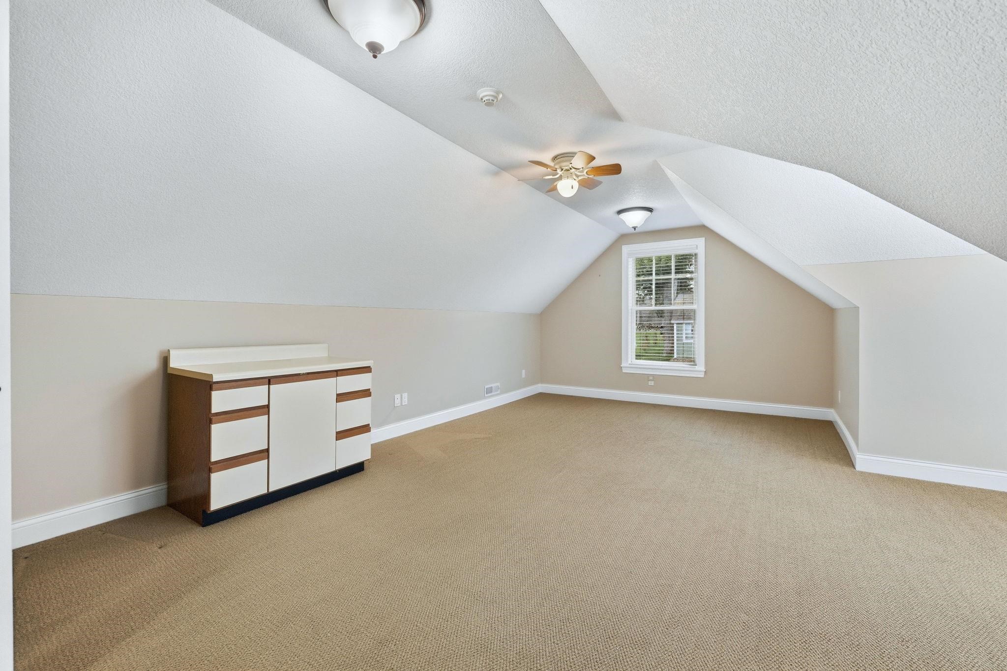 Bonus room with light colored carpet and a ceiling fan