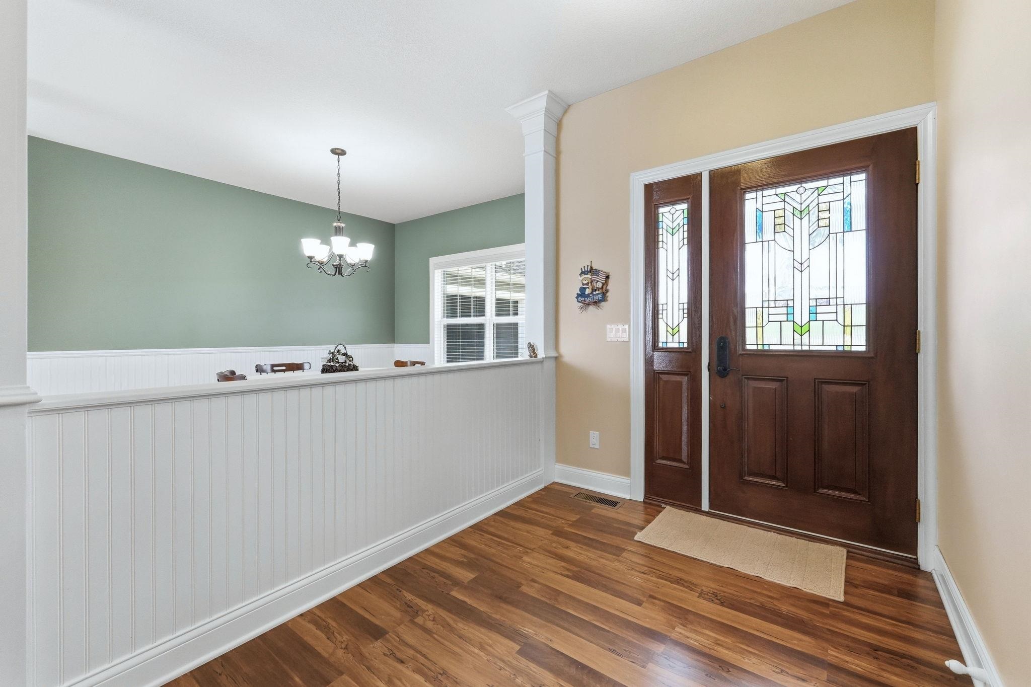 Foyer entrance featuring hanging lights, dark wood-style floors, and wainscoting