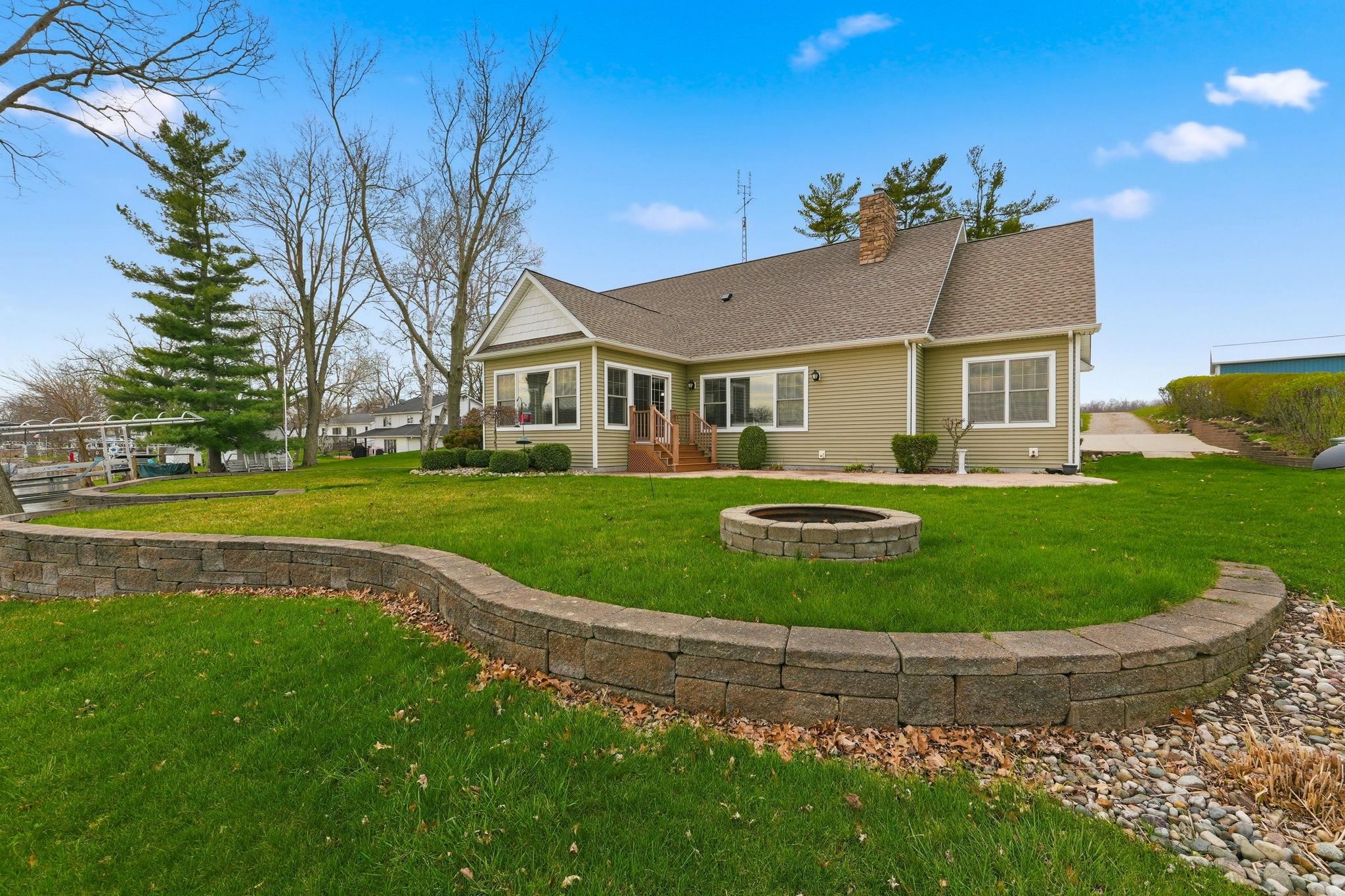 Rear view of property with a lawn, a chimney, a shingled roof, an outdoor fire pit, and a sunroom