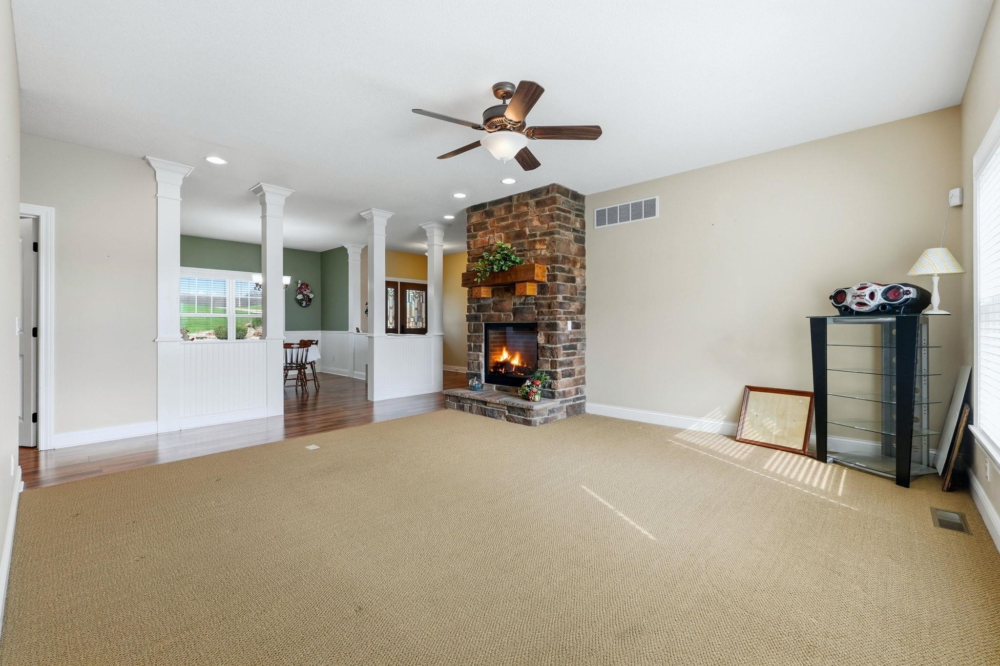Unfurnished living room featuring decorative columns, a fireplace, recessed lighting, a ceiling fan, and light carpet