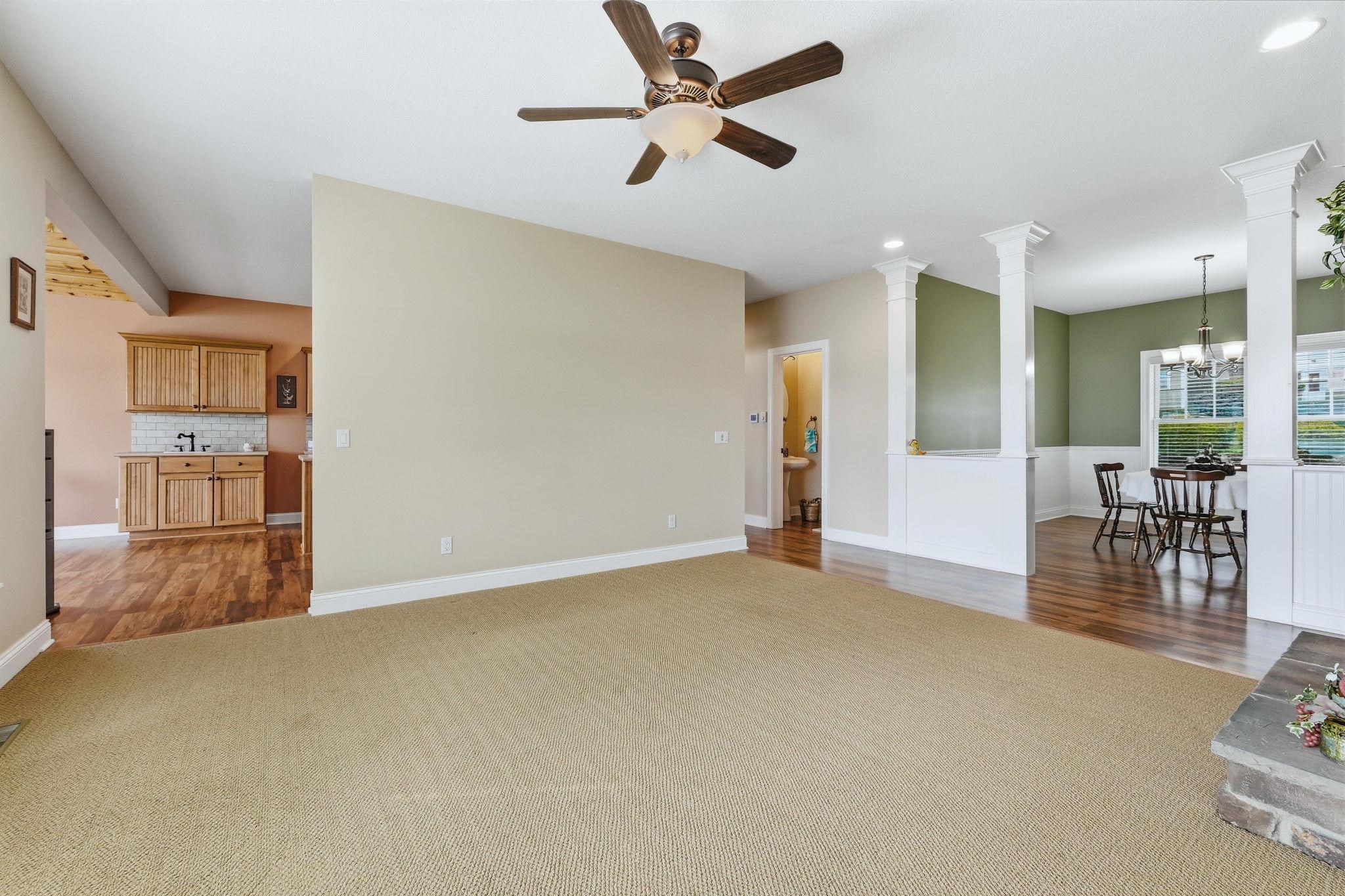 Living area with a ceiling fan, ornate columns, dark colored carpet, and hanging lights