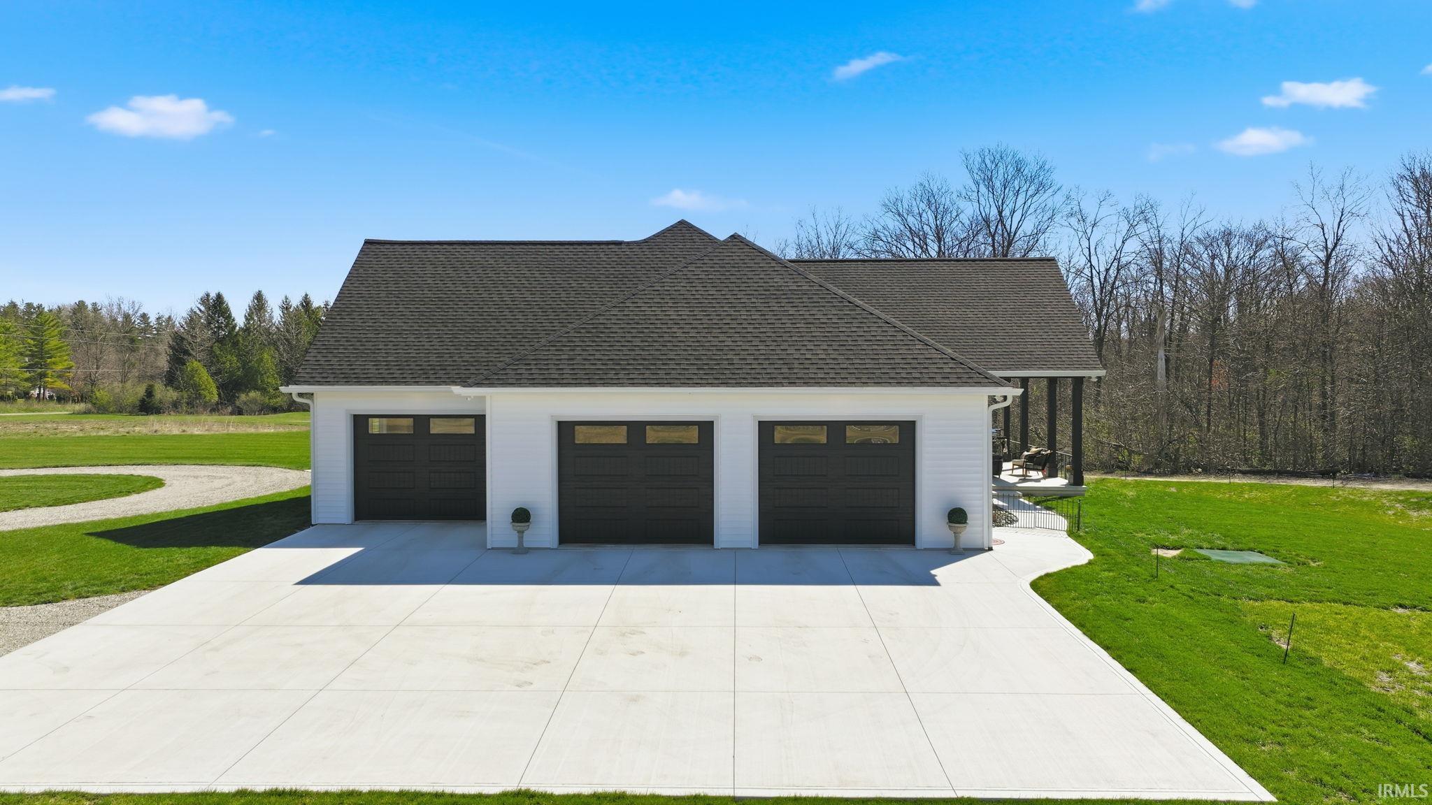 View of side of property with a lawn, concrete driveway, an attached garage, and a shingled roof