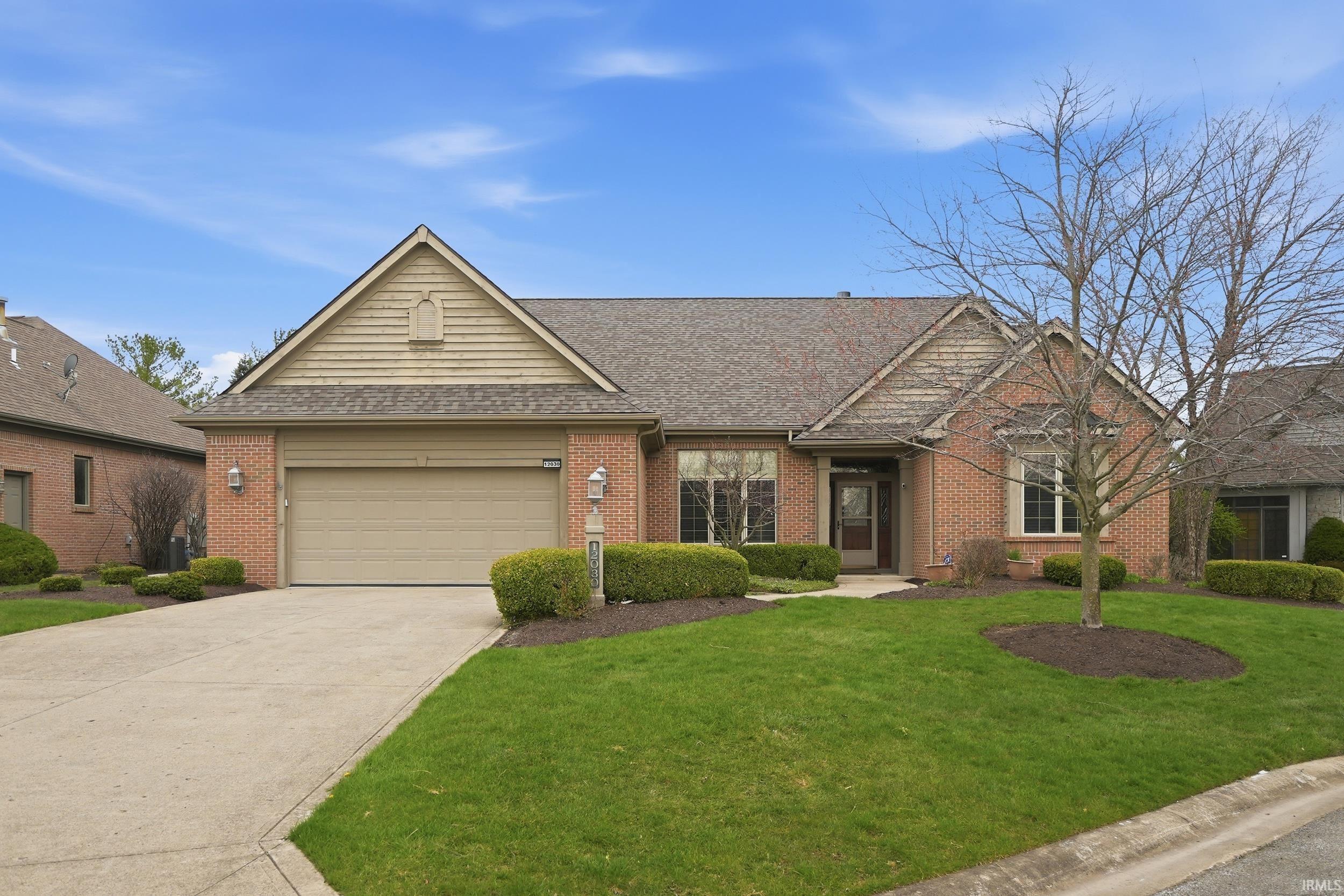 Ranch-style home with a shingled roof, brick siding, an attached garage, driveway, and a front lawn