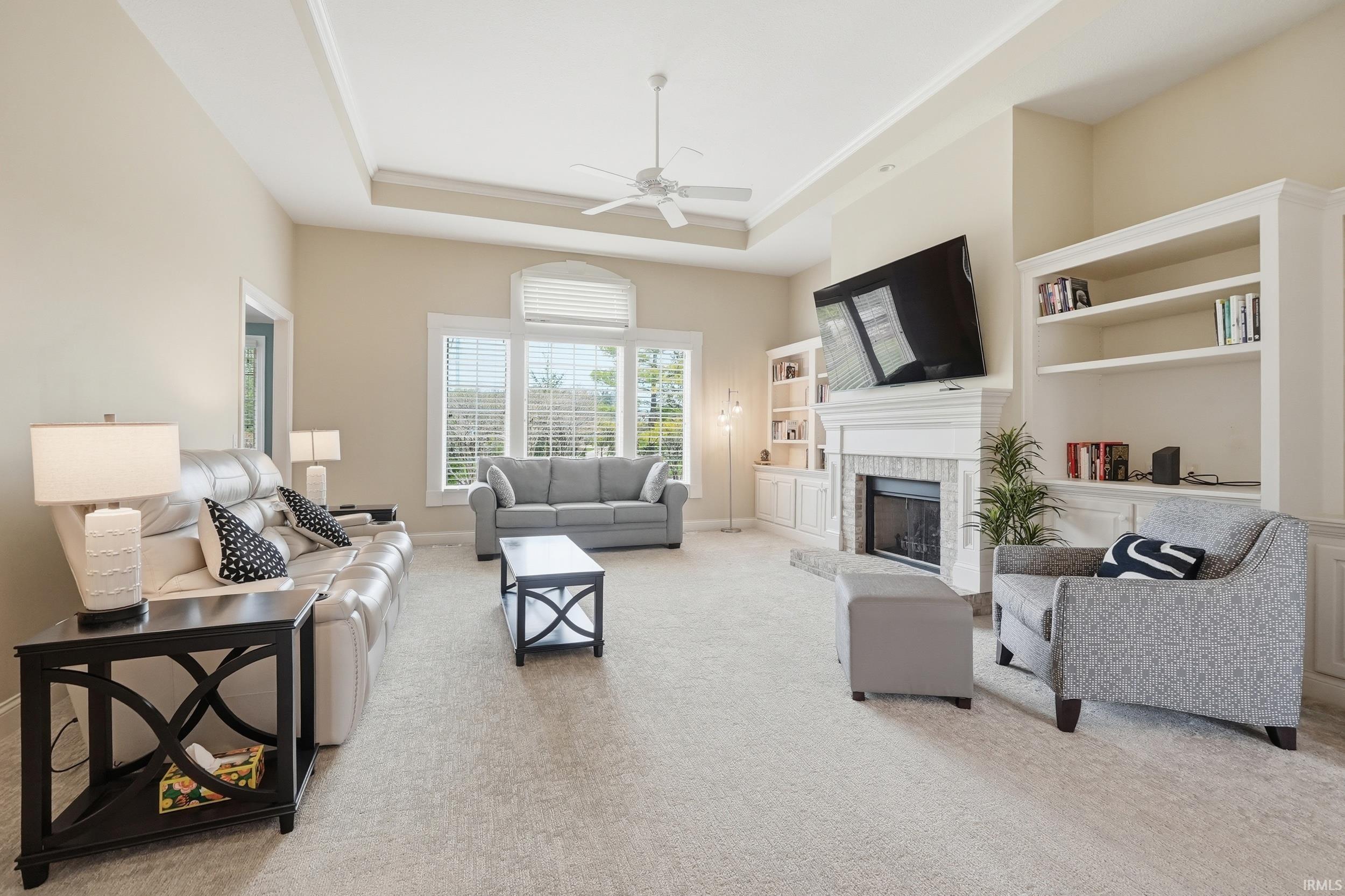 Living area featuring a ceiling fan, light carpet, a fireplace, built in shelves, and a raised ceiling
