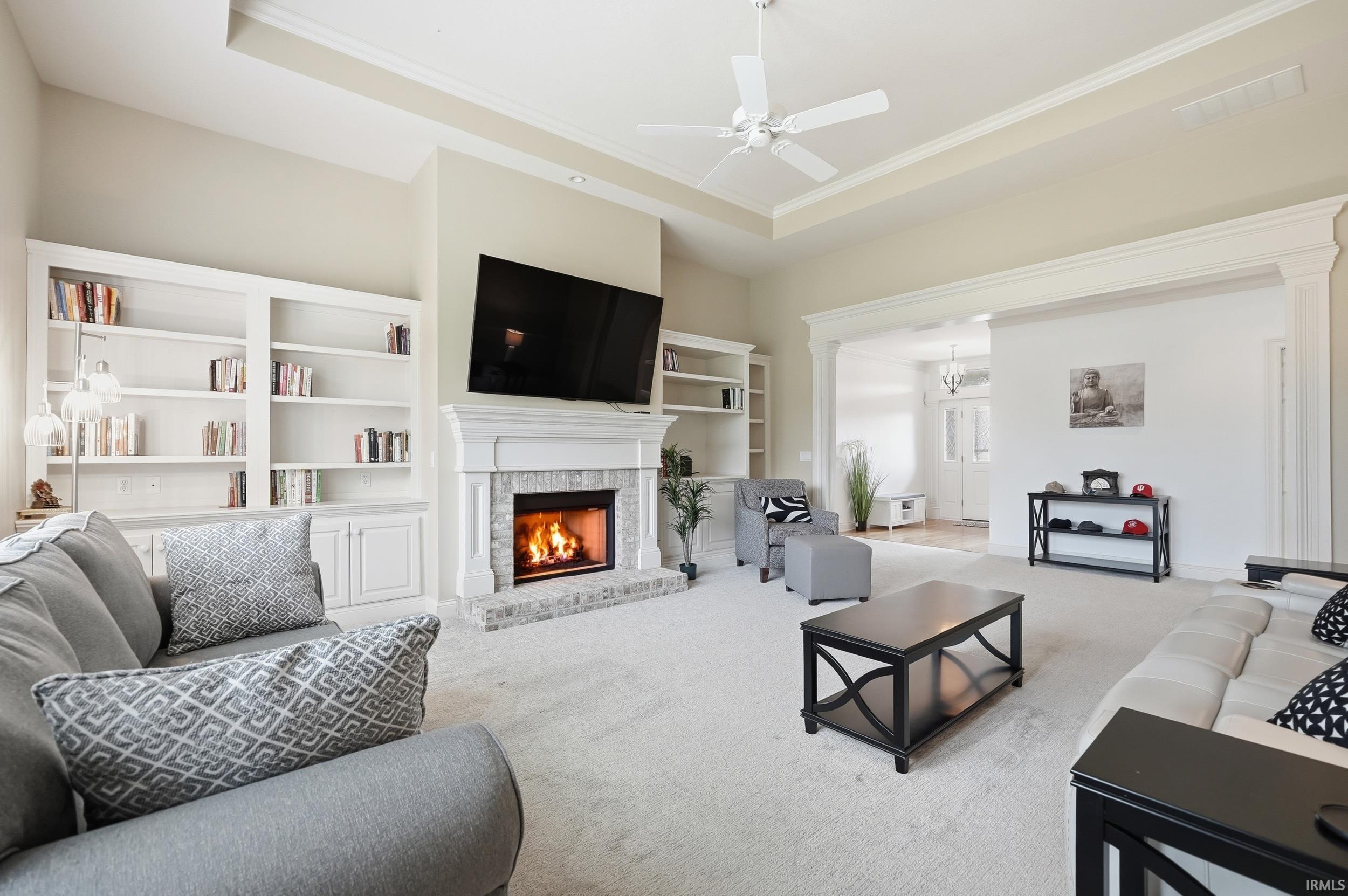Carpeted living area featuring a raised ceiling, a ceiling fan, a fireplace, and ornamental molding