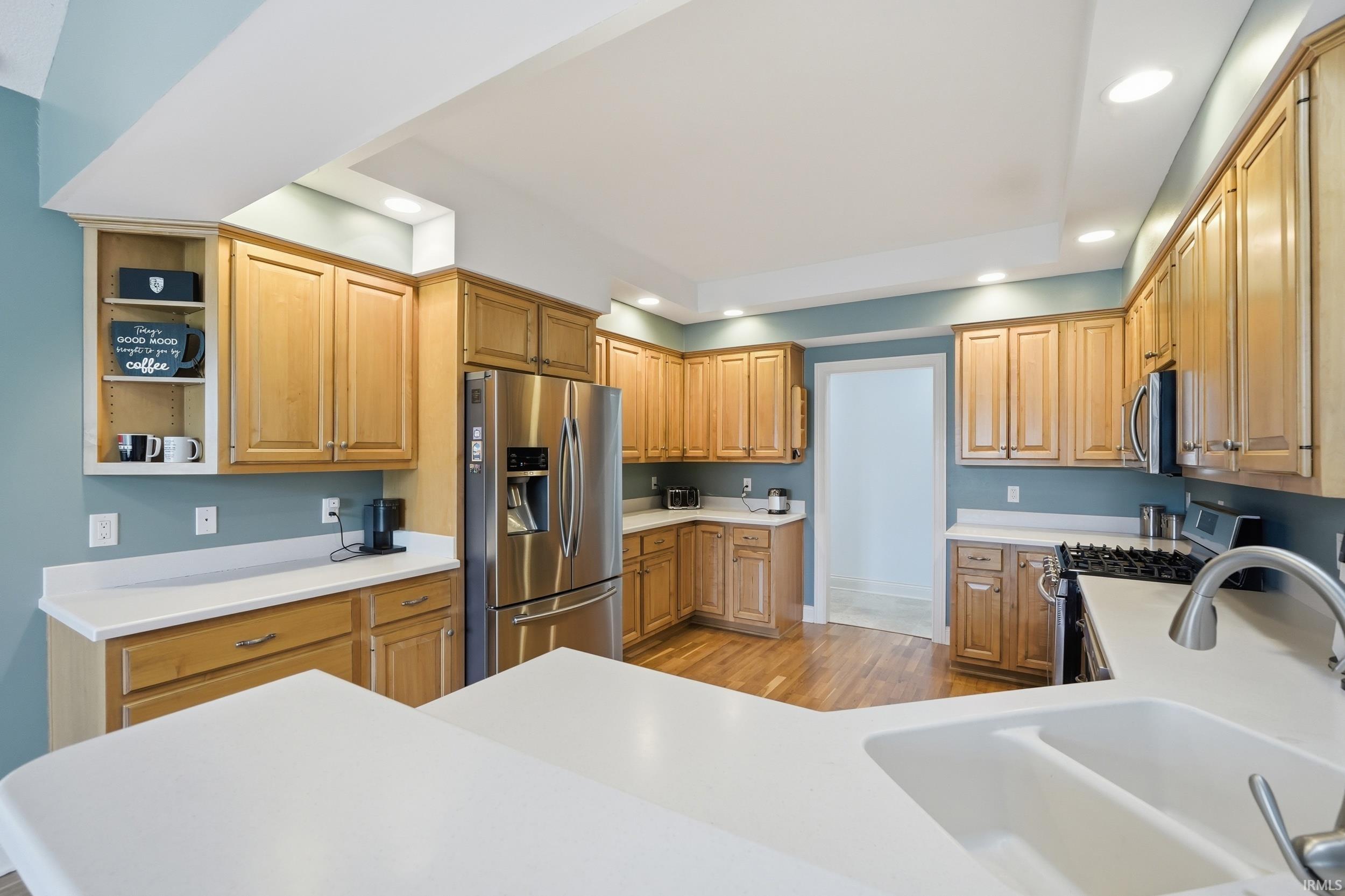 Kitchen featuring stainless steel appliances, open shelves, light countertops, light wood finished floors, and recessed lighting
