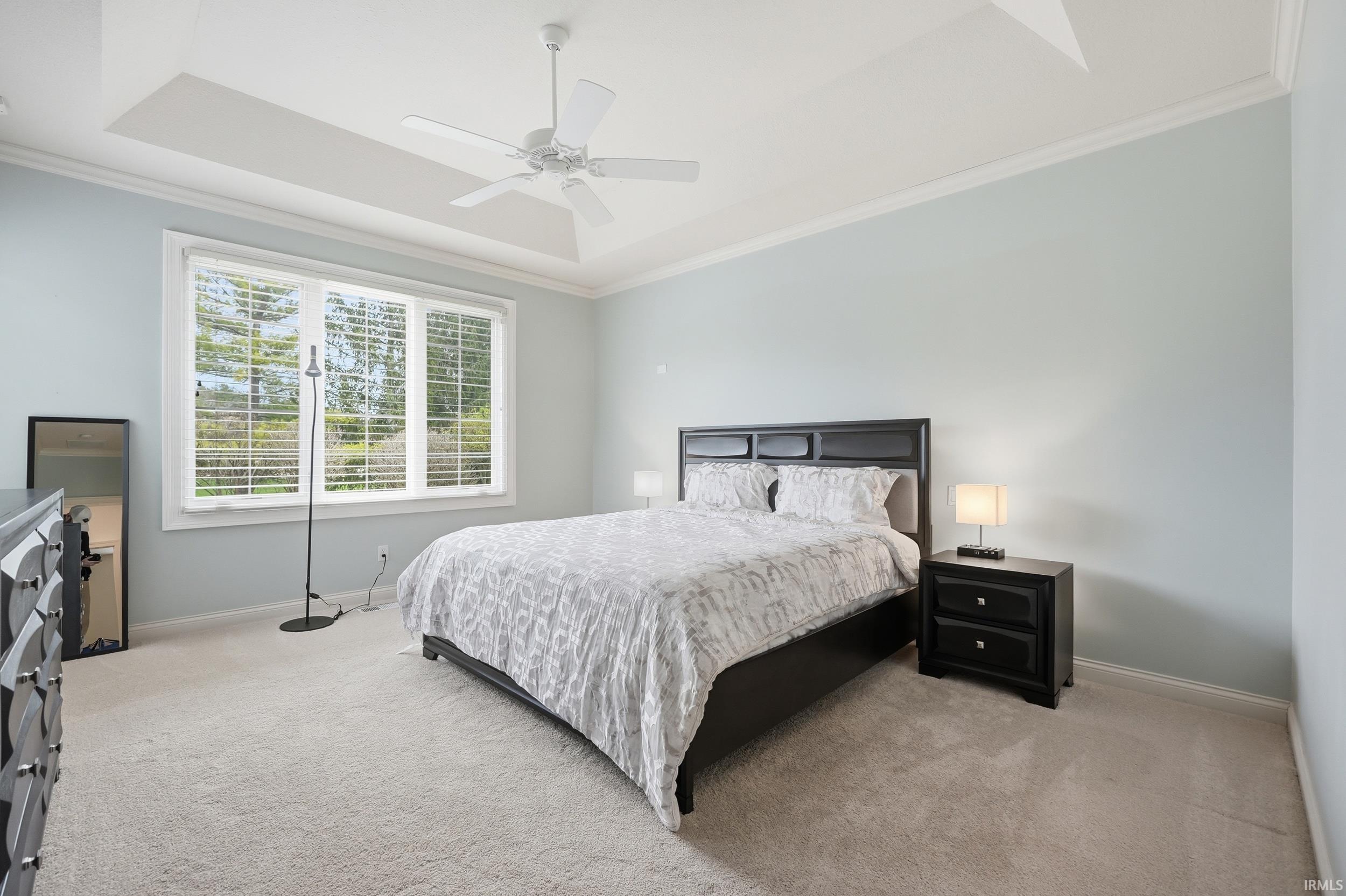 Bedroom with crown molding, light carpet, ceiling fan, and a tray ceiling