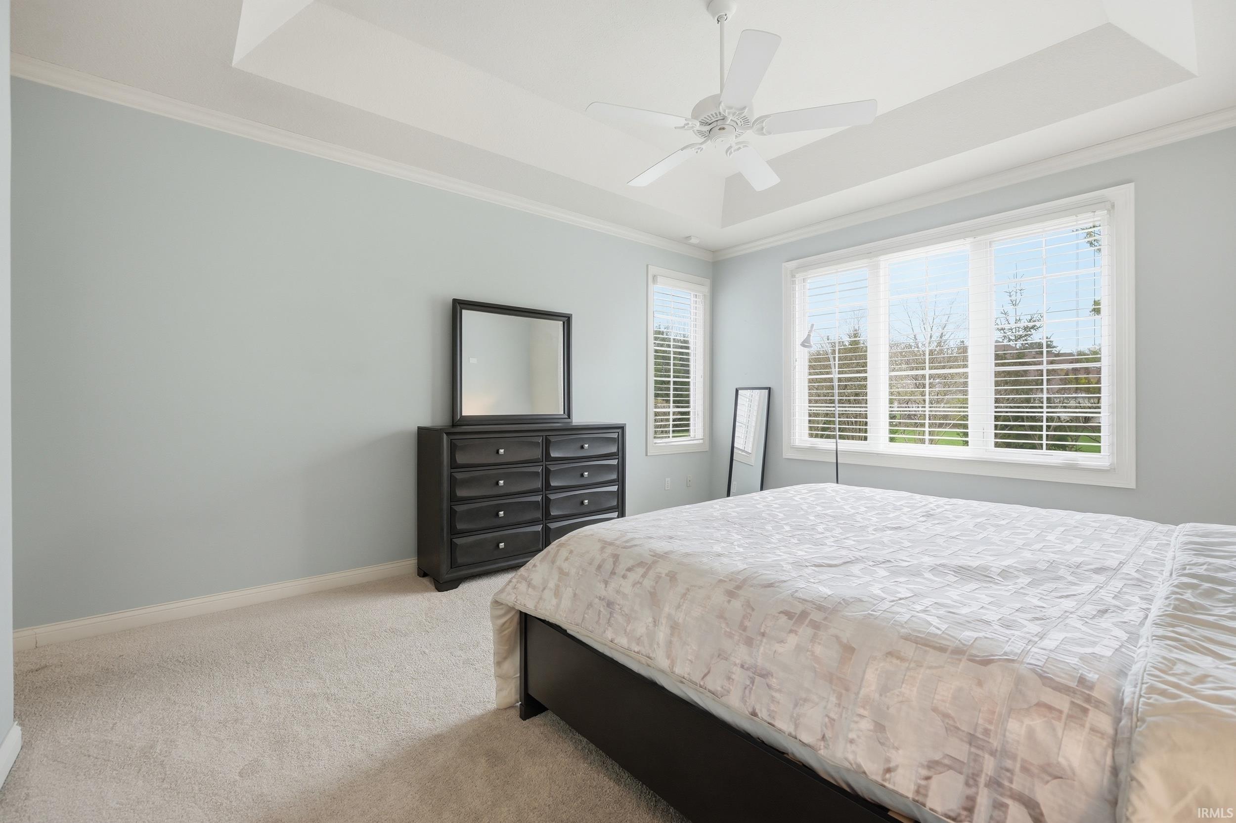 Bedroom with light carpet, crown molding, ceiling fan, and a tray ceiling
