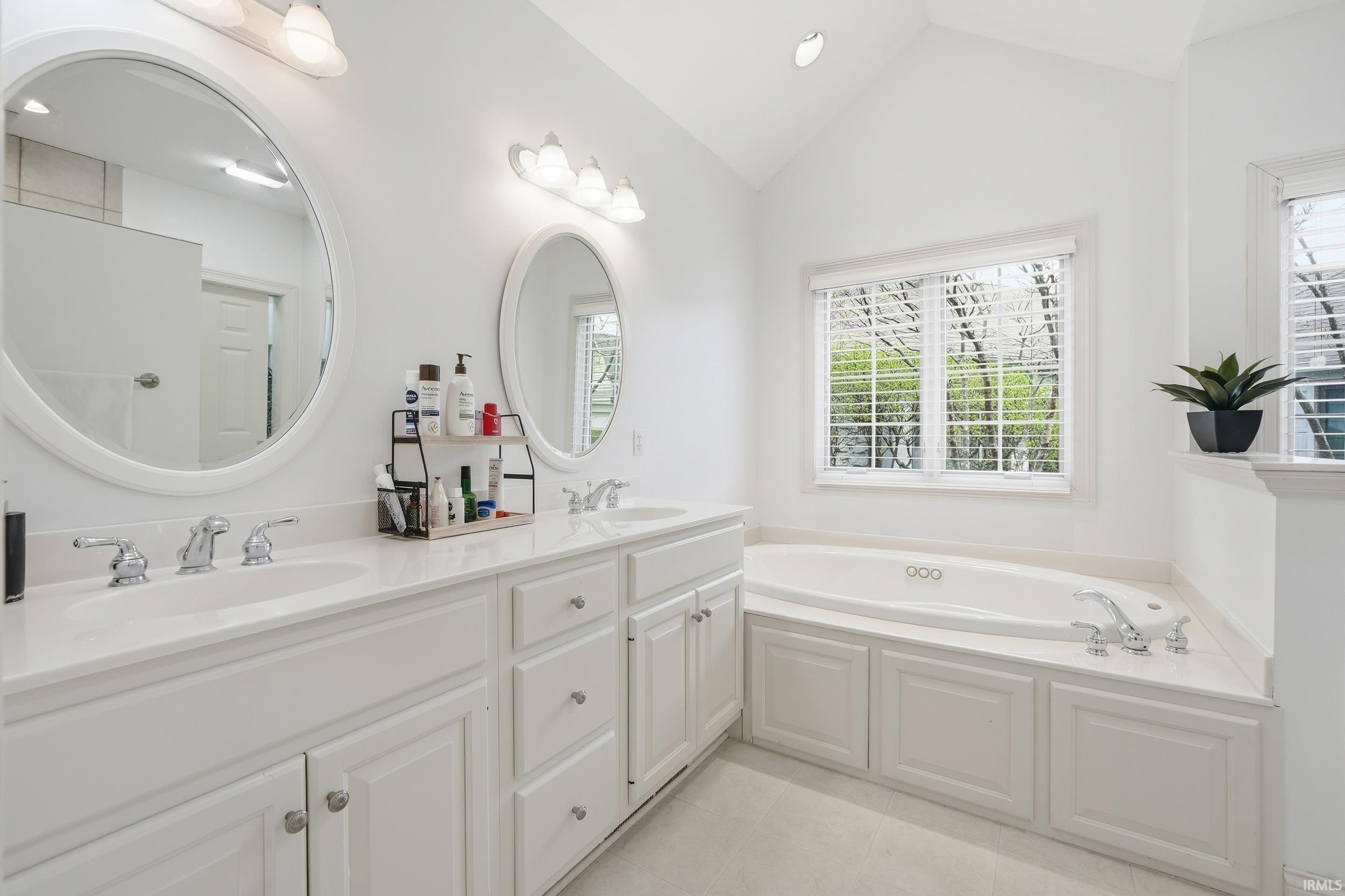 Full bathroom featuring double vanity, a garden tub, light tile patterned flooring, recessed lighting, and vaulted ceiling