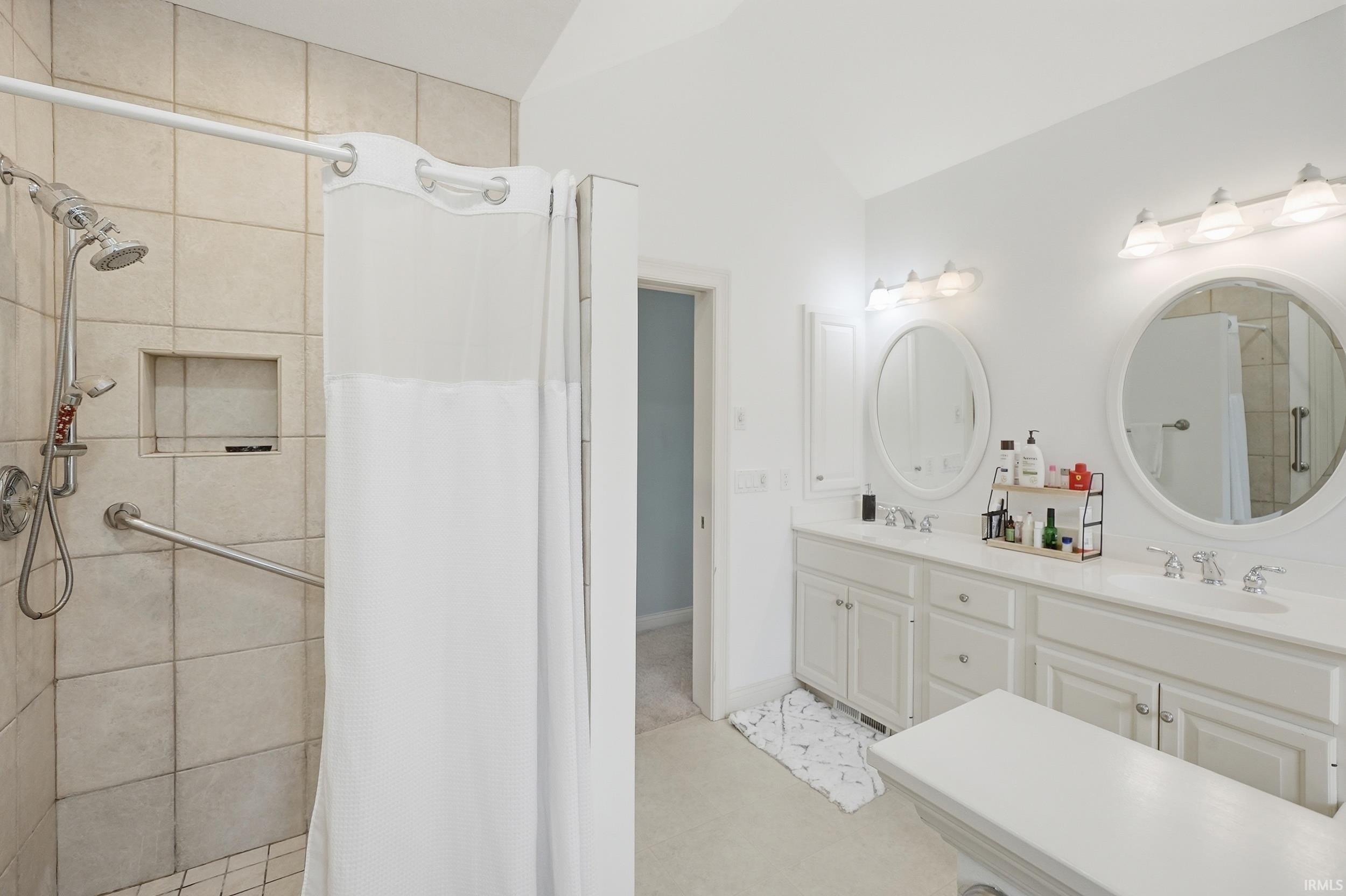 Bathroom featuring double vanity, a shower stall, and vaulted ceiling