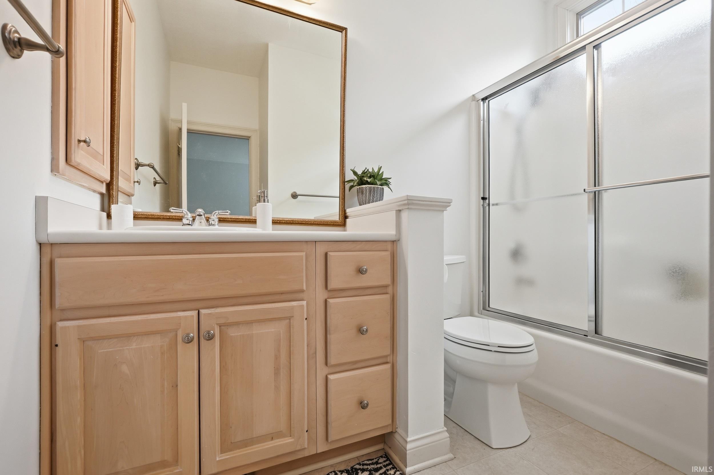 Bathroom with vanity, bath / shower combo with glass door, and light tile patterned floors
