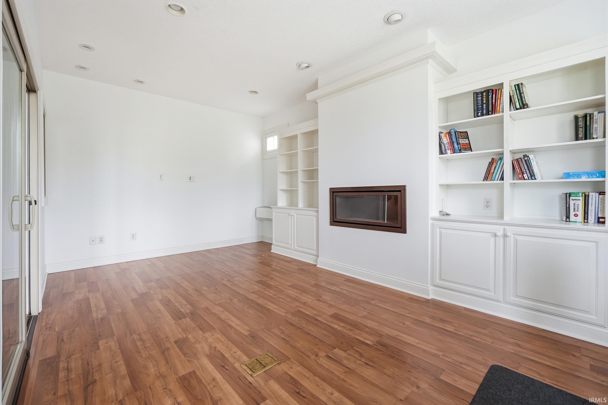 Unfurnished living room featuring built in features, dark wood-type flooring, a glass covered fireplace, and recessed lighting