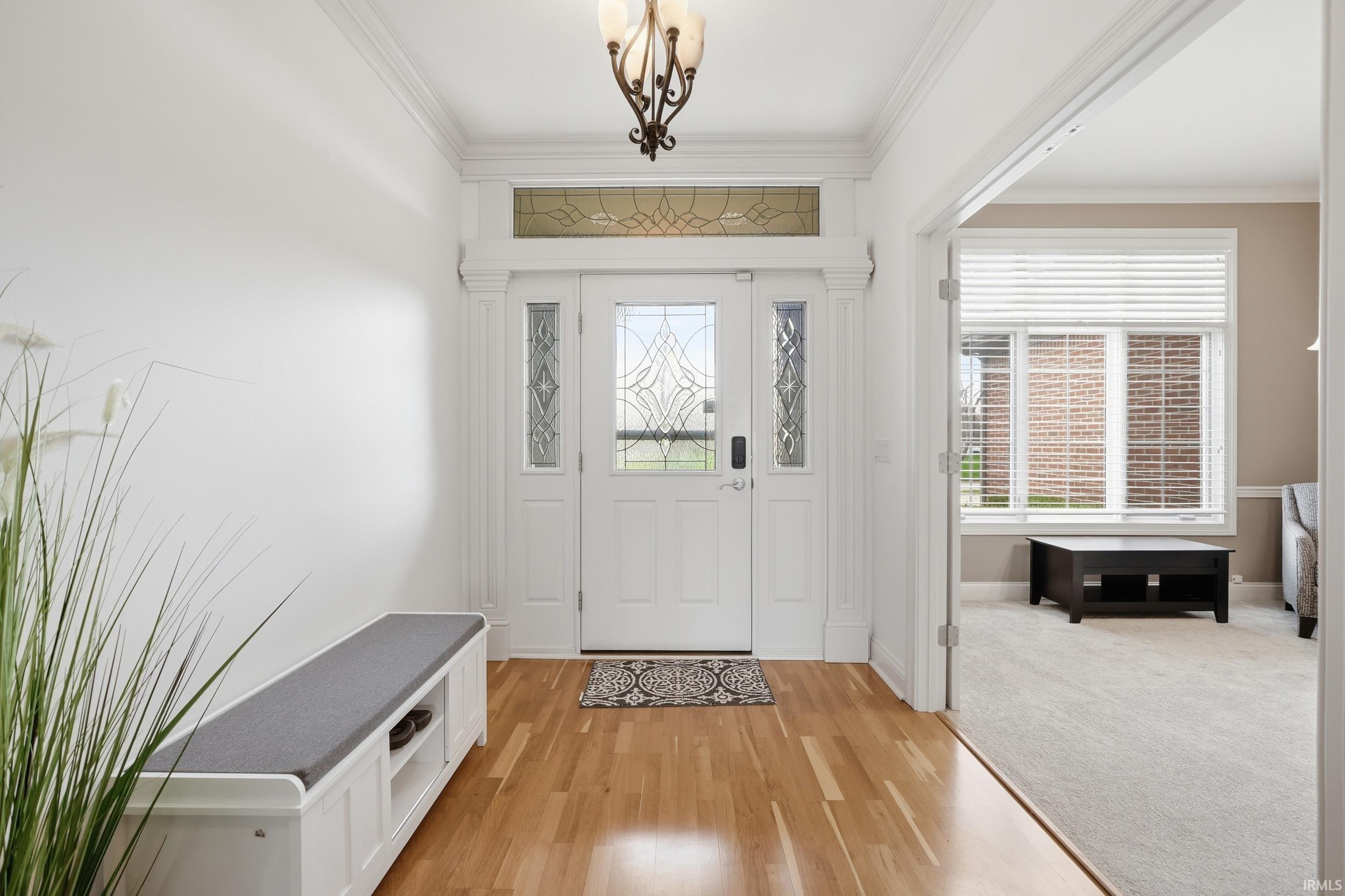 Entrance foyer with ornamental molding, light wood-style flooring, and hanging lights