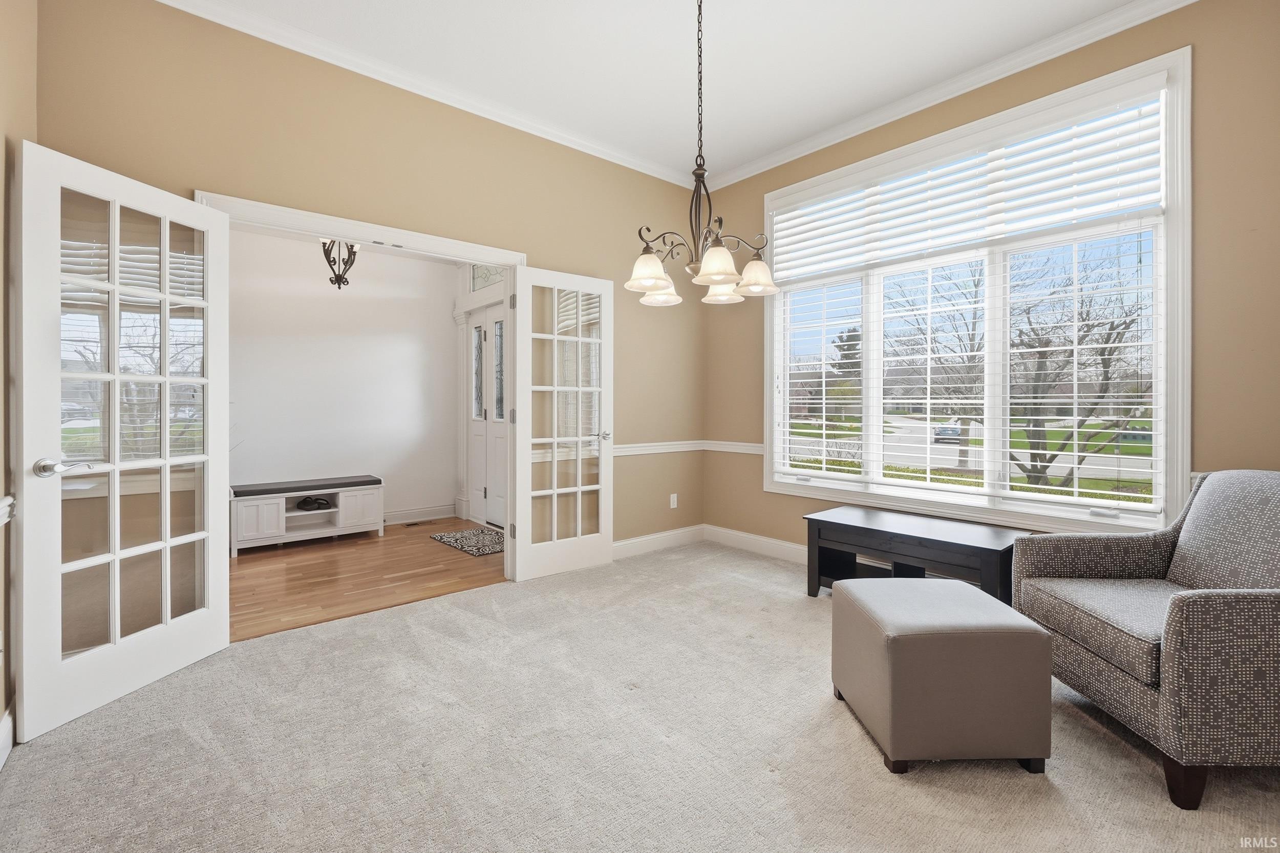 Living area with ornamental molding, light colored carpet, and hanging lights