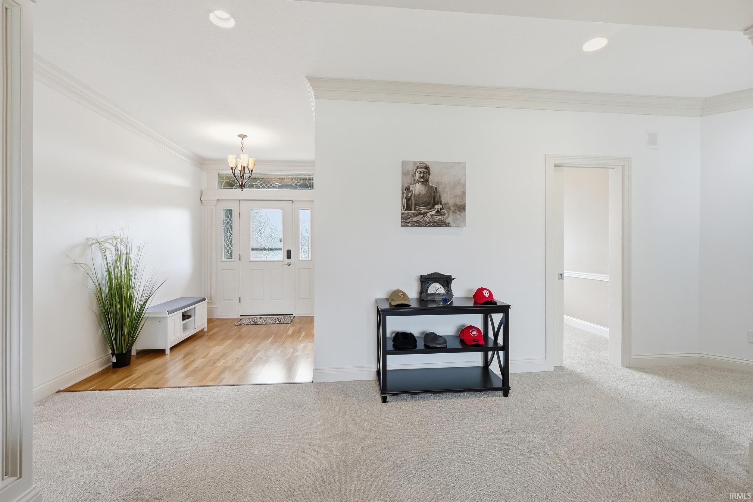 Entryway with ornamental molding, light colored carpet, and a chandelier
