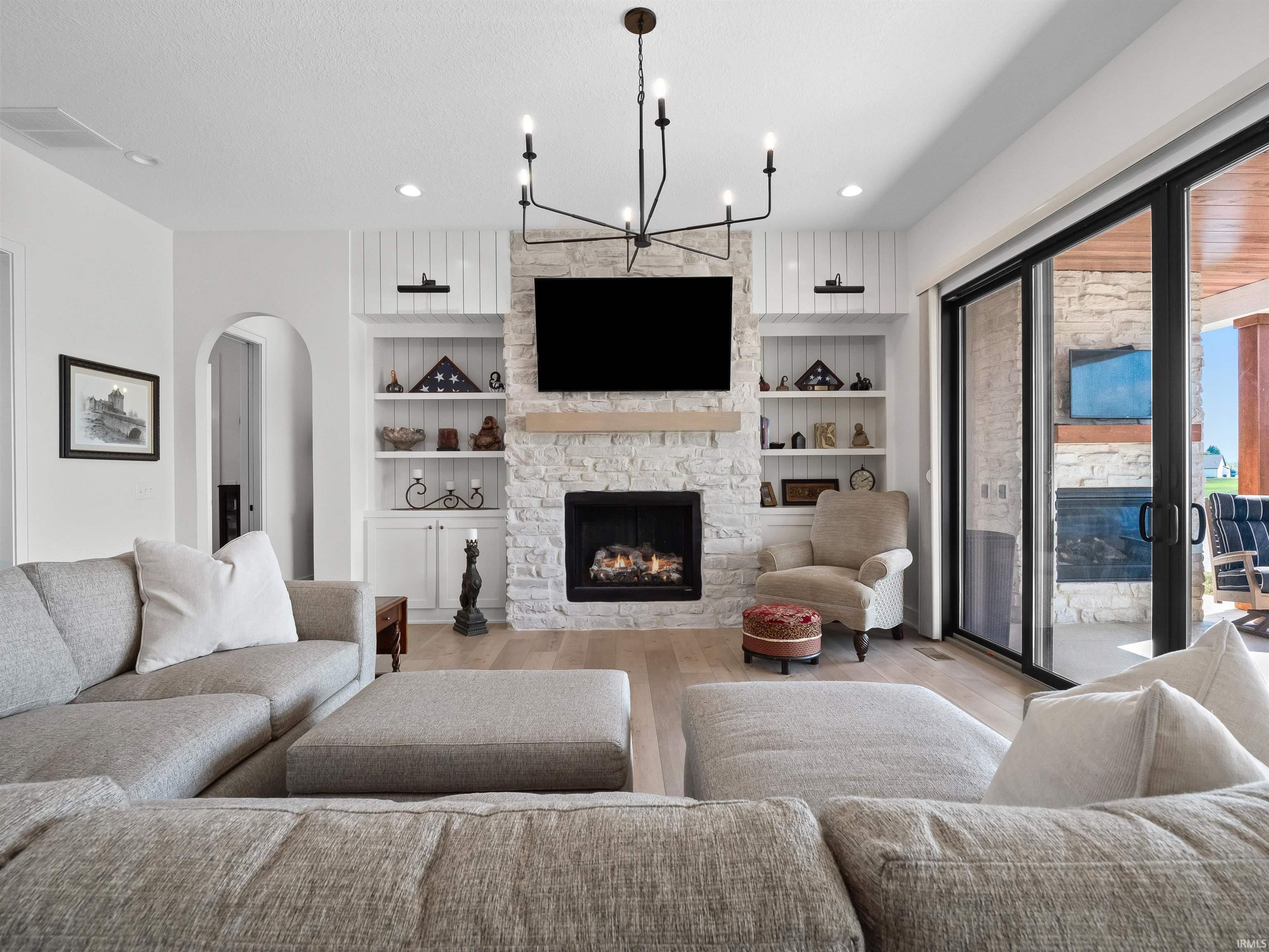 Living area with wood finished floors, arched walkways, a stone fireplace, a chandelier, and built in features