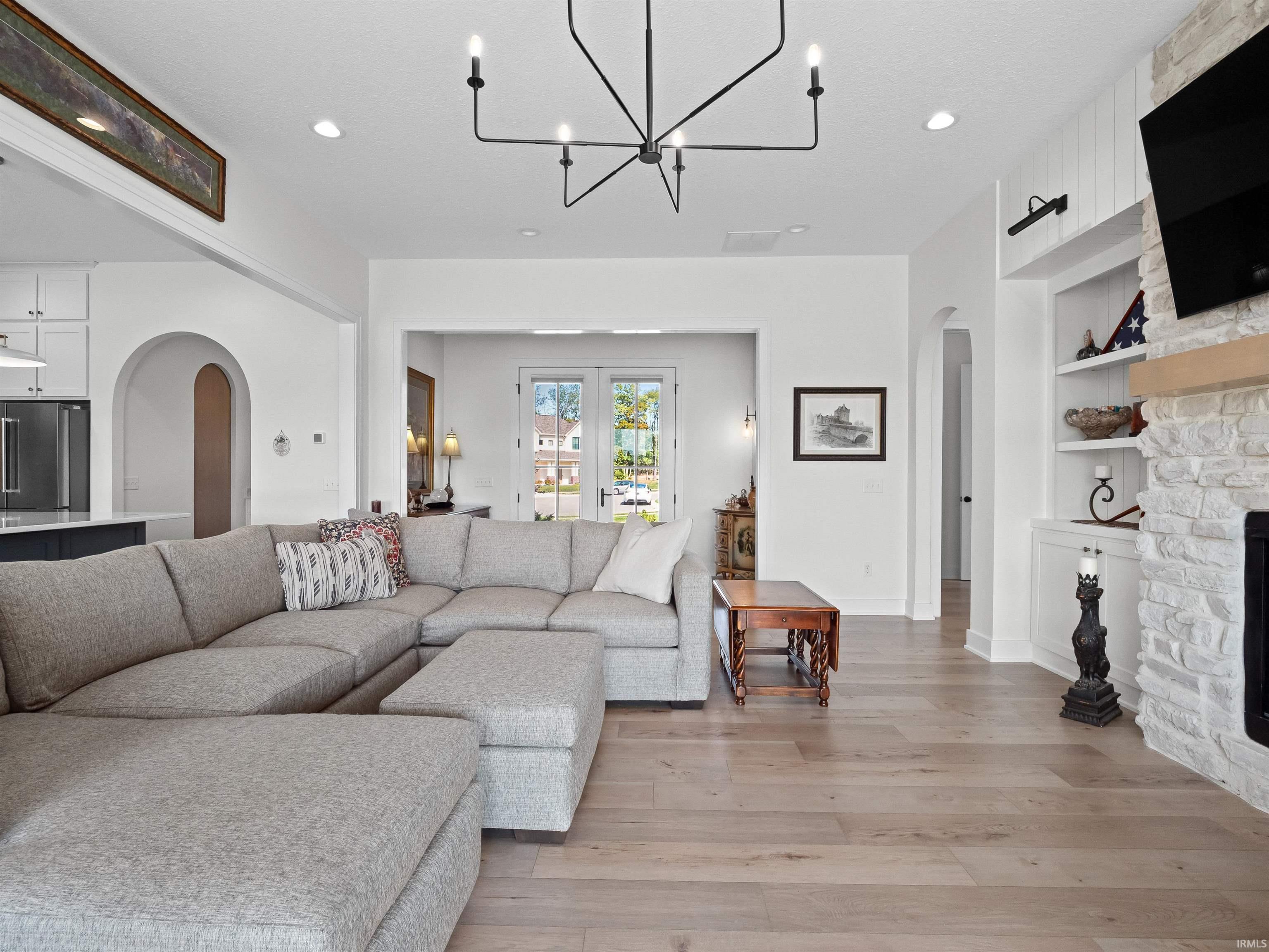 Living area featuring arched walkways, built in shelves, light wood-style flooring, a fireplace, and a chandelier