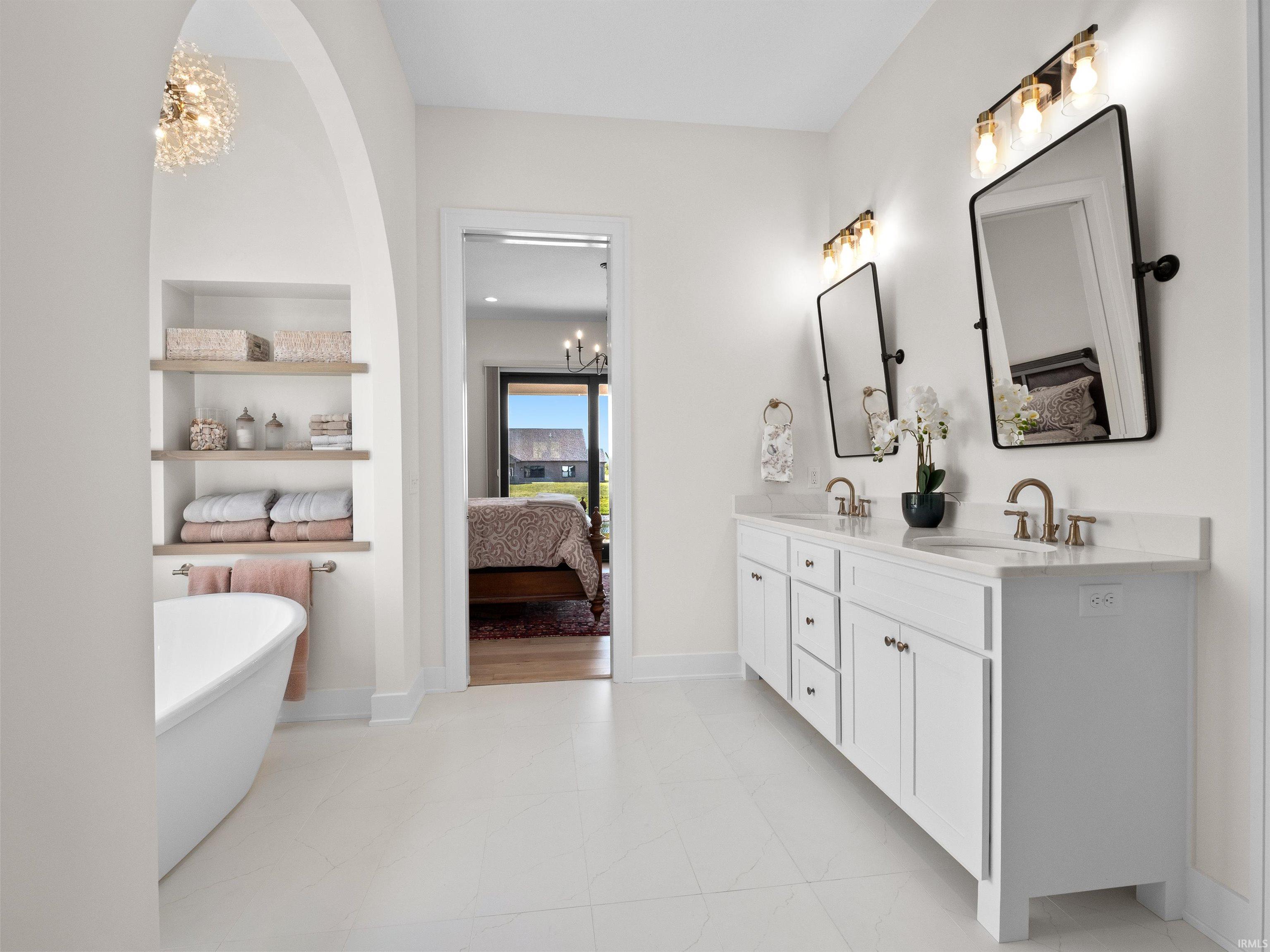 Bathroom with connected bathroom, a chandelier, double vanity, and a soaking tub