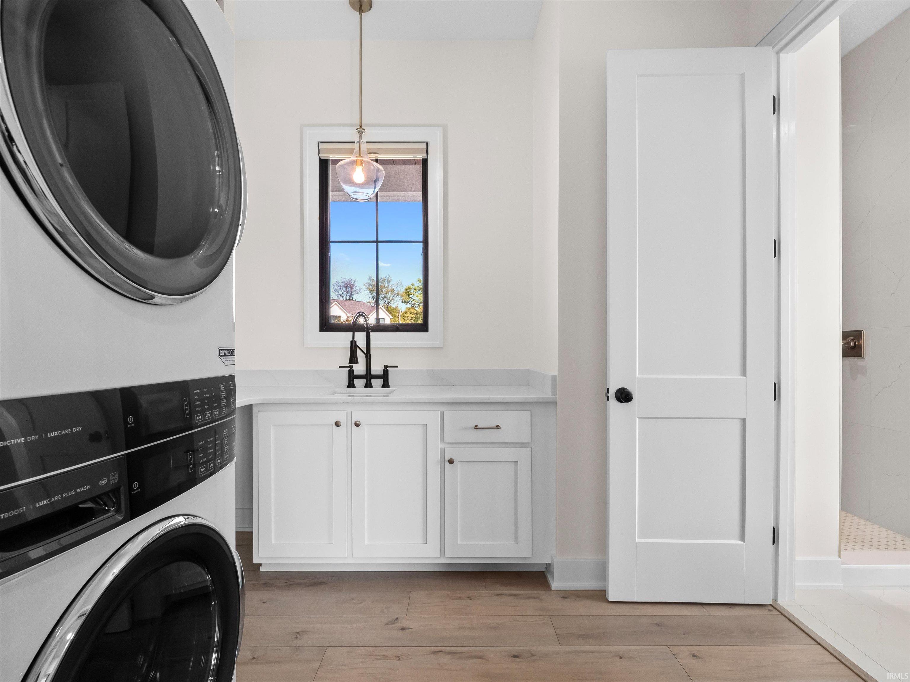Washroom with stacked washer and clothes dryer, cabinet space, and light wood-type flooring