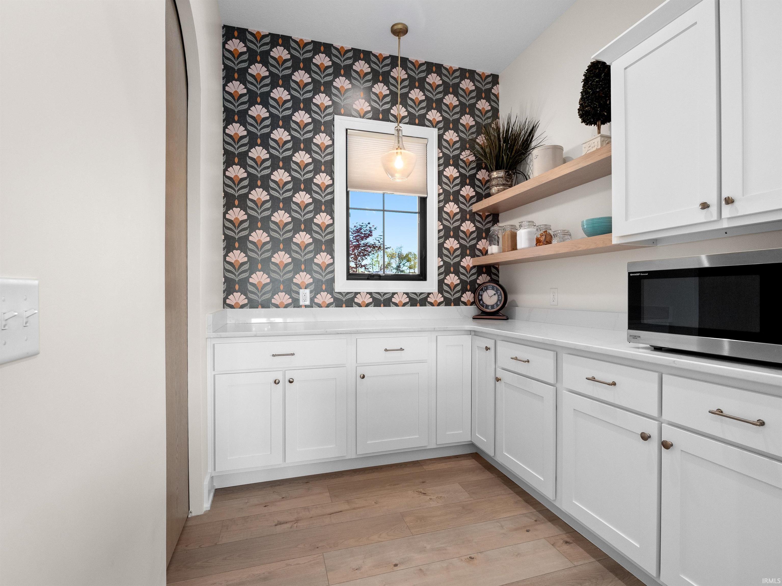 Kitchen featuring open shelves, white cabinetry, stainless steel microwave, decorative light fixtures, and wallpapered walls