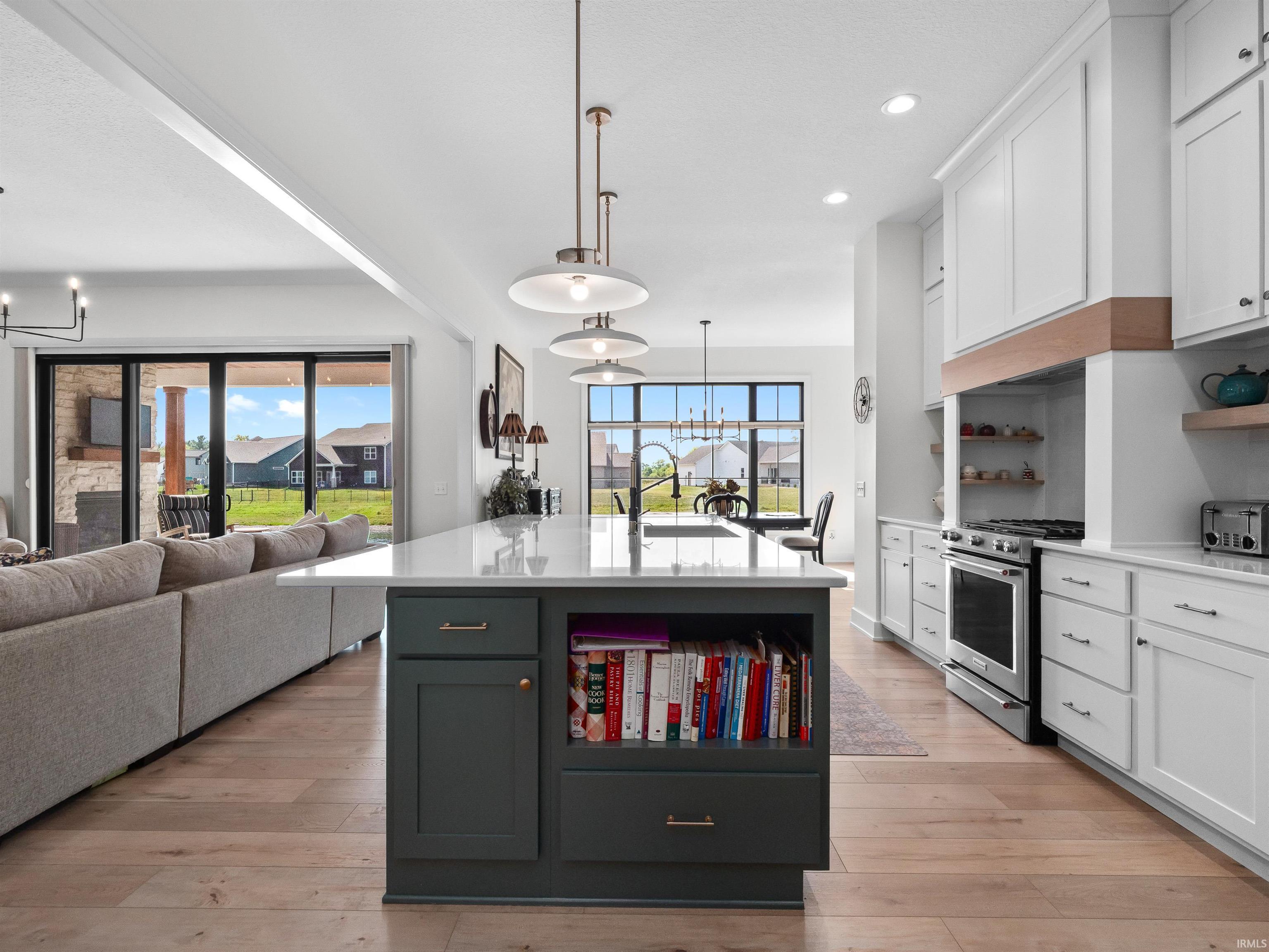 Kitchen with a chandelier, white cabinetry, open shelves, an island with sink, and recessed lighting