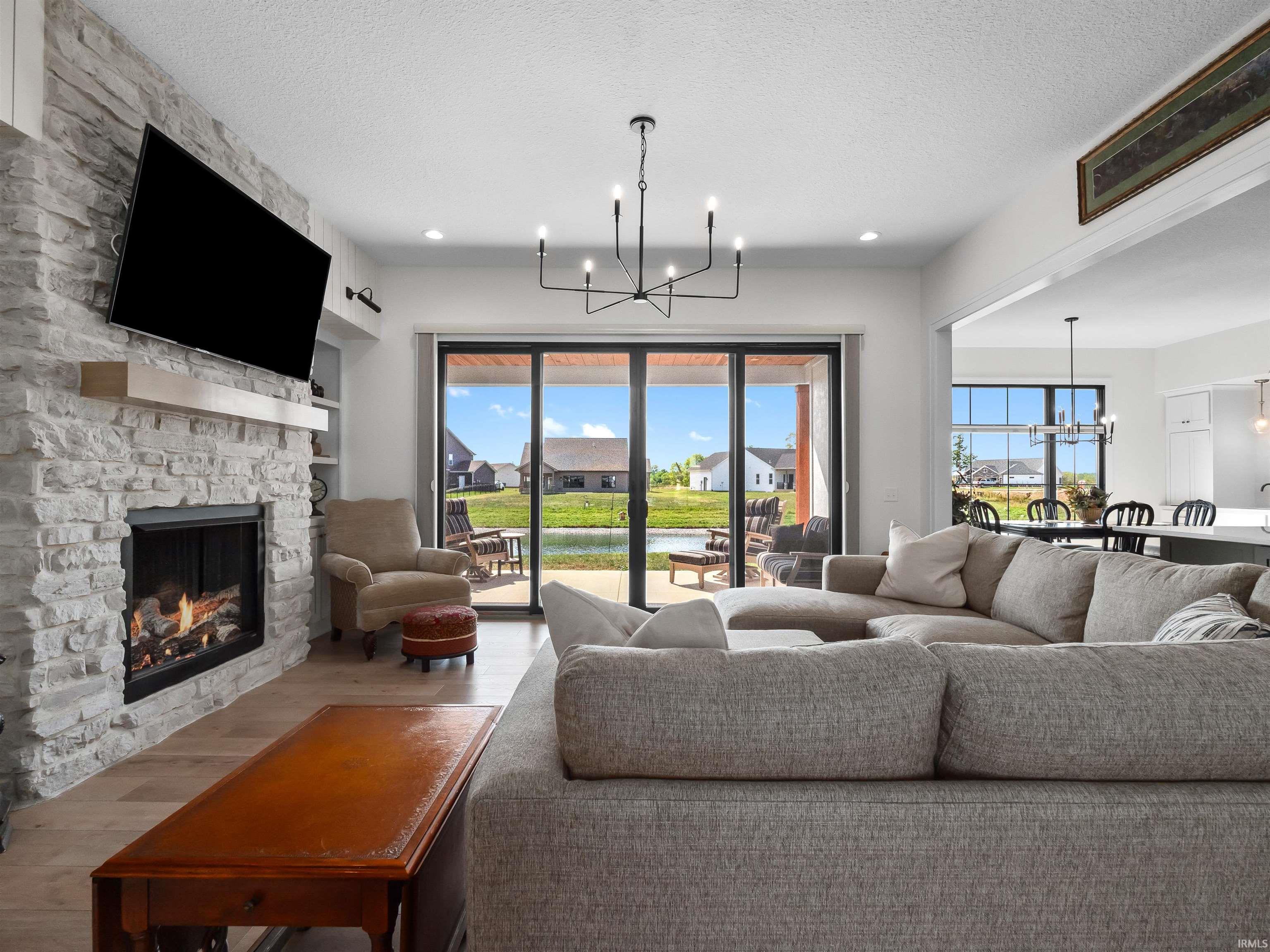 Living room featuring a chandelier, a stone fireplace, wood finished floors, a textured ceiling, and recessed lighting