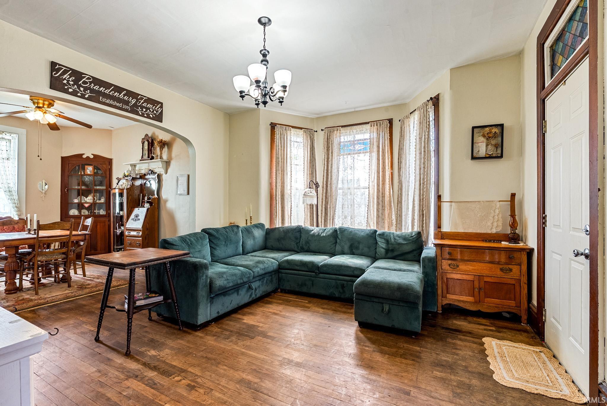 Living area featuring dark wood-style flooring, a ceiling fan, arched walkways, and suspended lighting