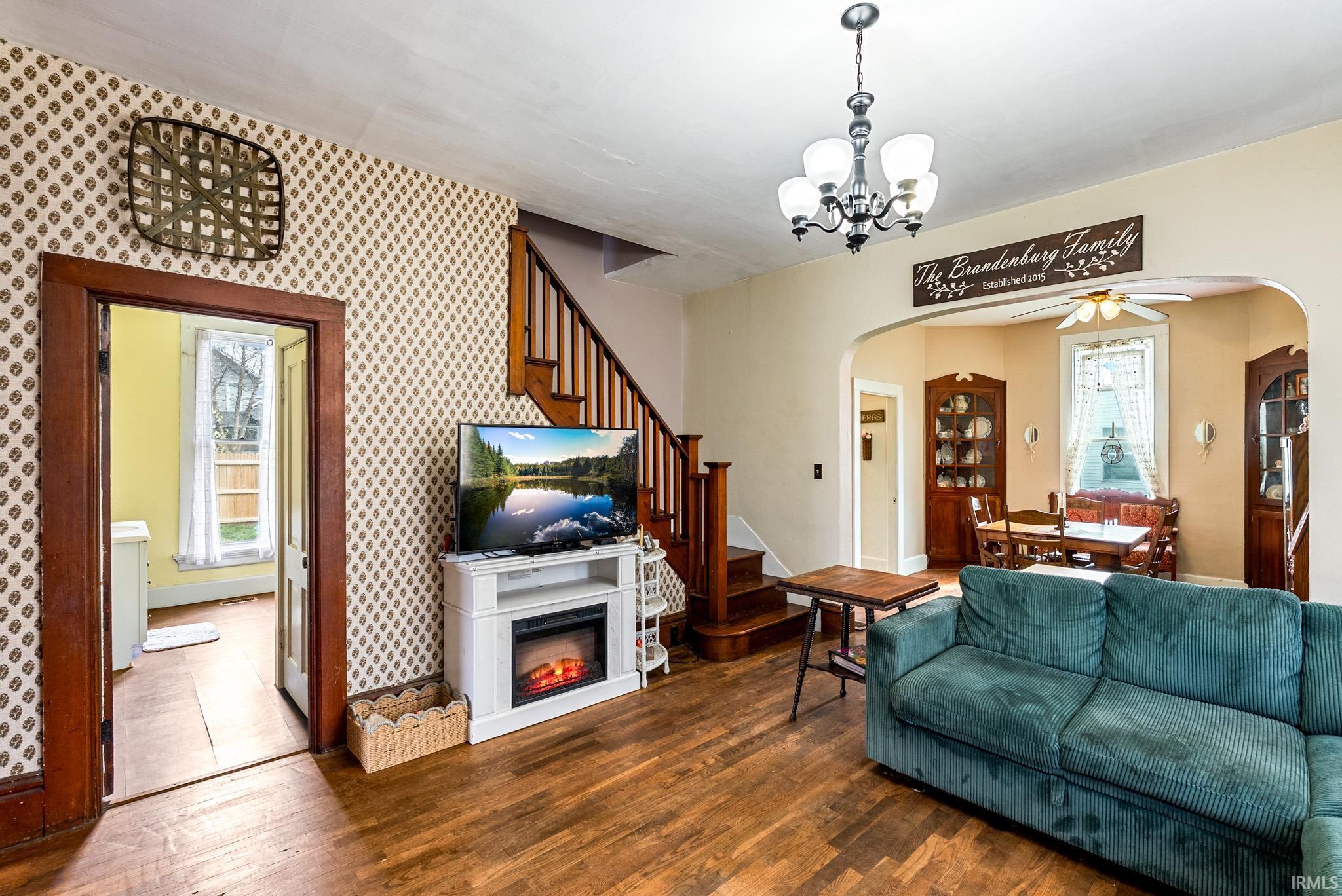 Living room featuring plenty of natural light, dark wood-style floors, a ceiling fan, suspended lighting, and wallpapered walls