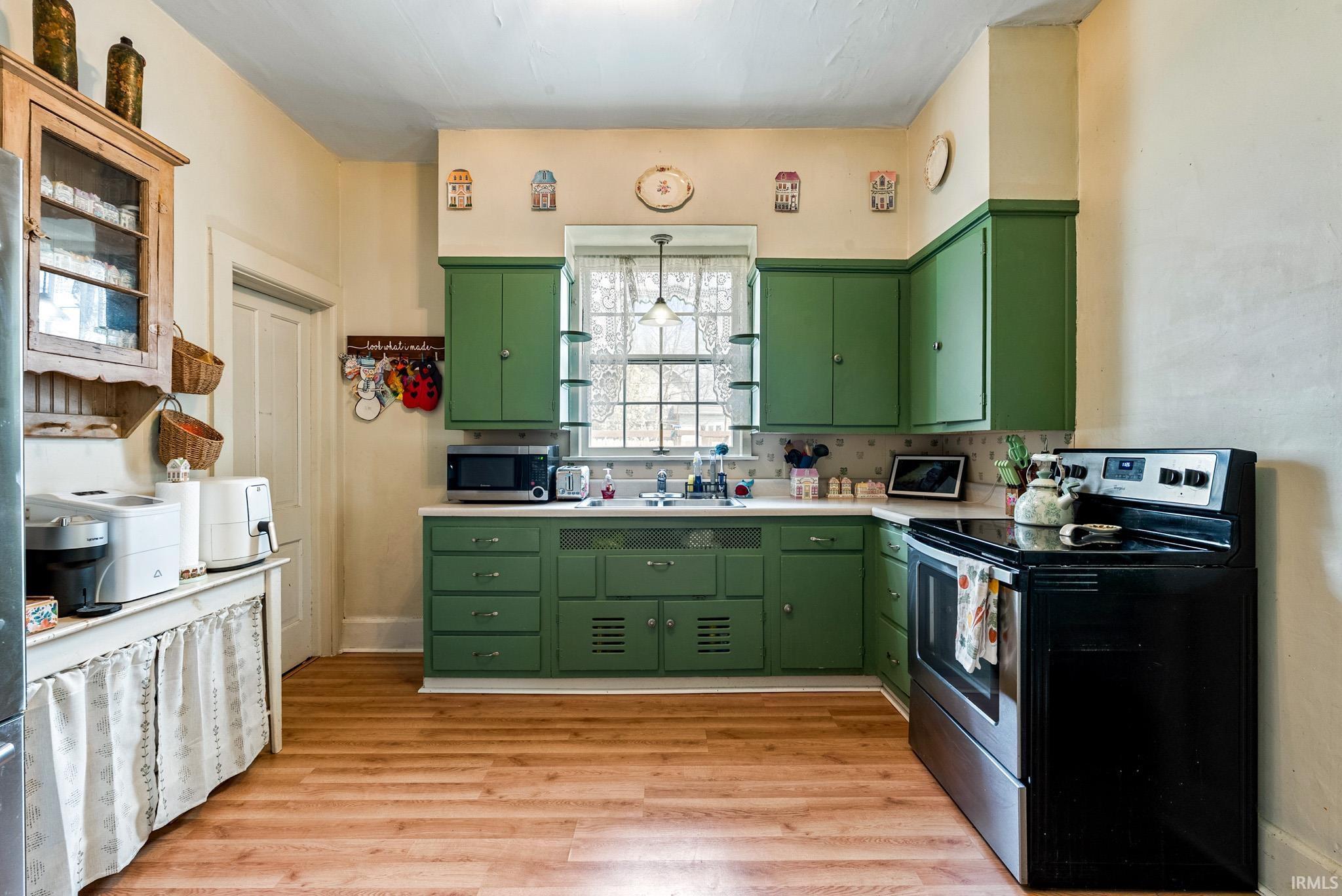 Kitchen with stainless steel appliances, light countertops, light wood-style floors, green cabinets, and pendant lighting