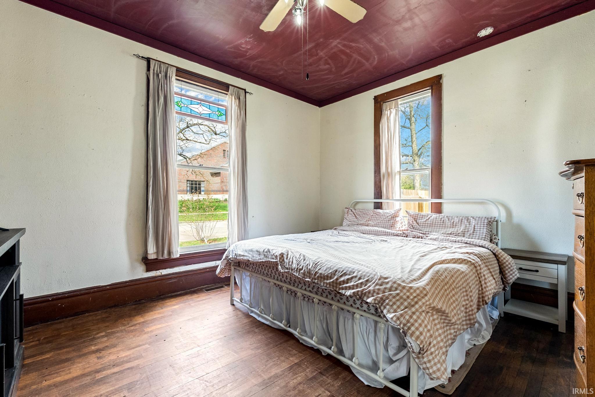 Bedroom featuring dark wood-style floors, ceiling fan, and multiple windows