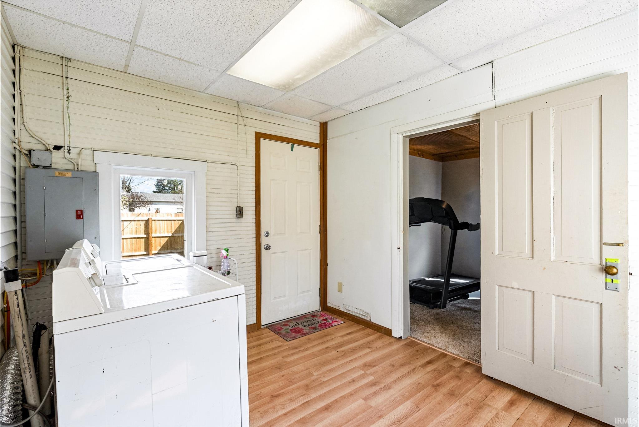 Laundry room featuring a drop ceiling, light wood-style floors, wood walls, electric panel, and independent washer and dryer