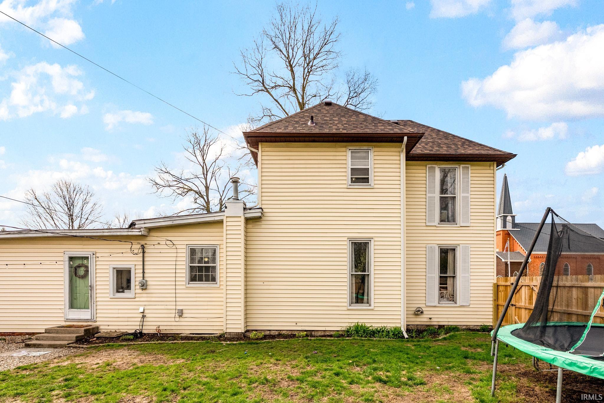 Rear view of property featuring a trampoline, a yard, entry steps, and roof with shingles