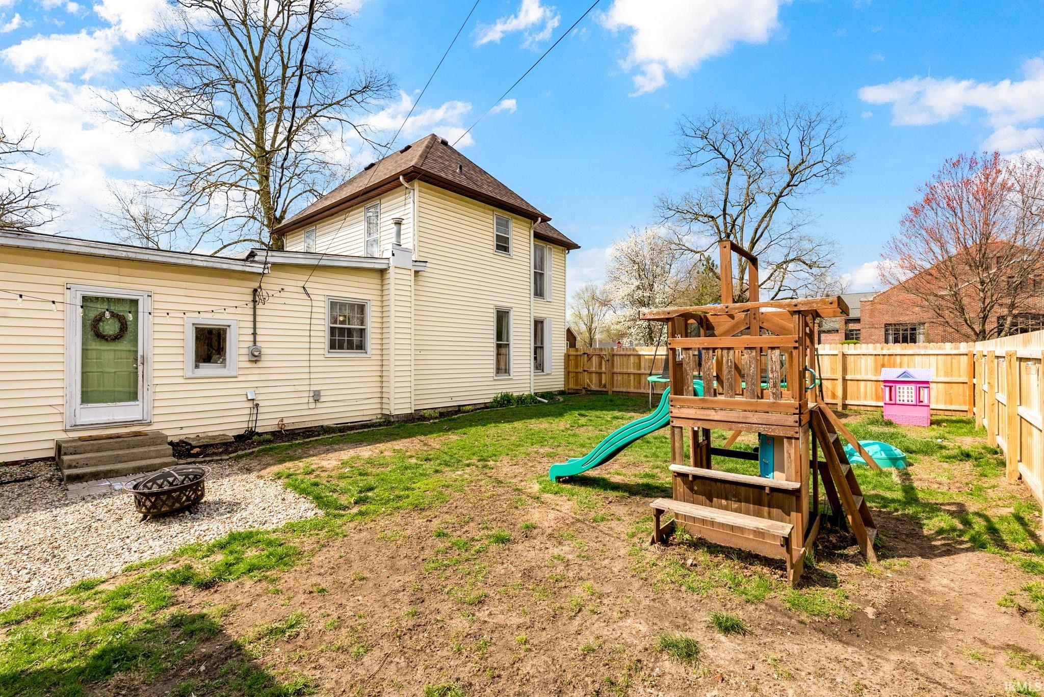 Rear view of house featuring entry steps, a fenced backyard, and an outdoor fire pit