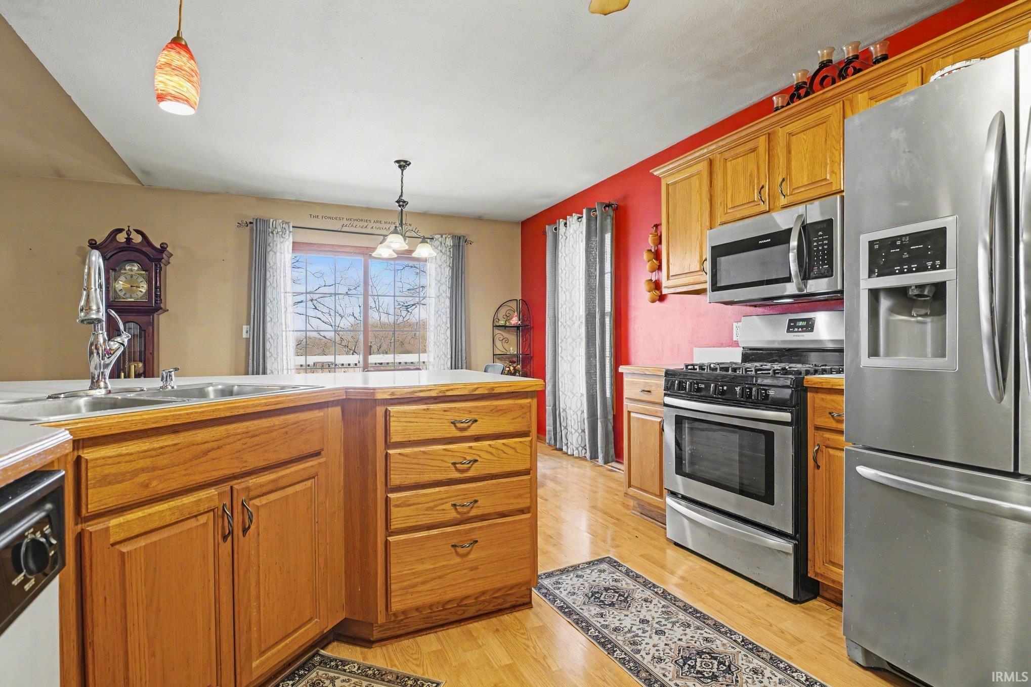 Kitchen featuring stainless steel appliances, light countertops, wood finish cabinetry, pendant lighting, and light wood-type flooring