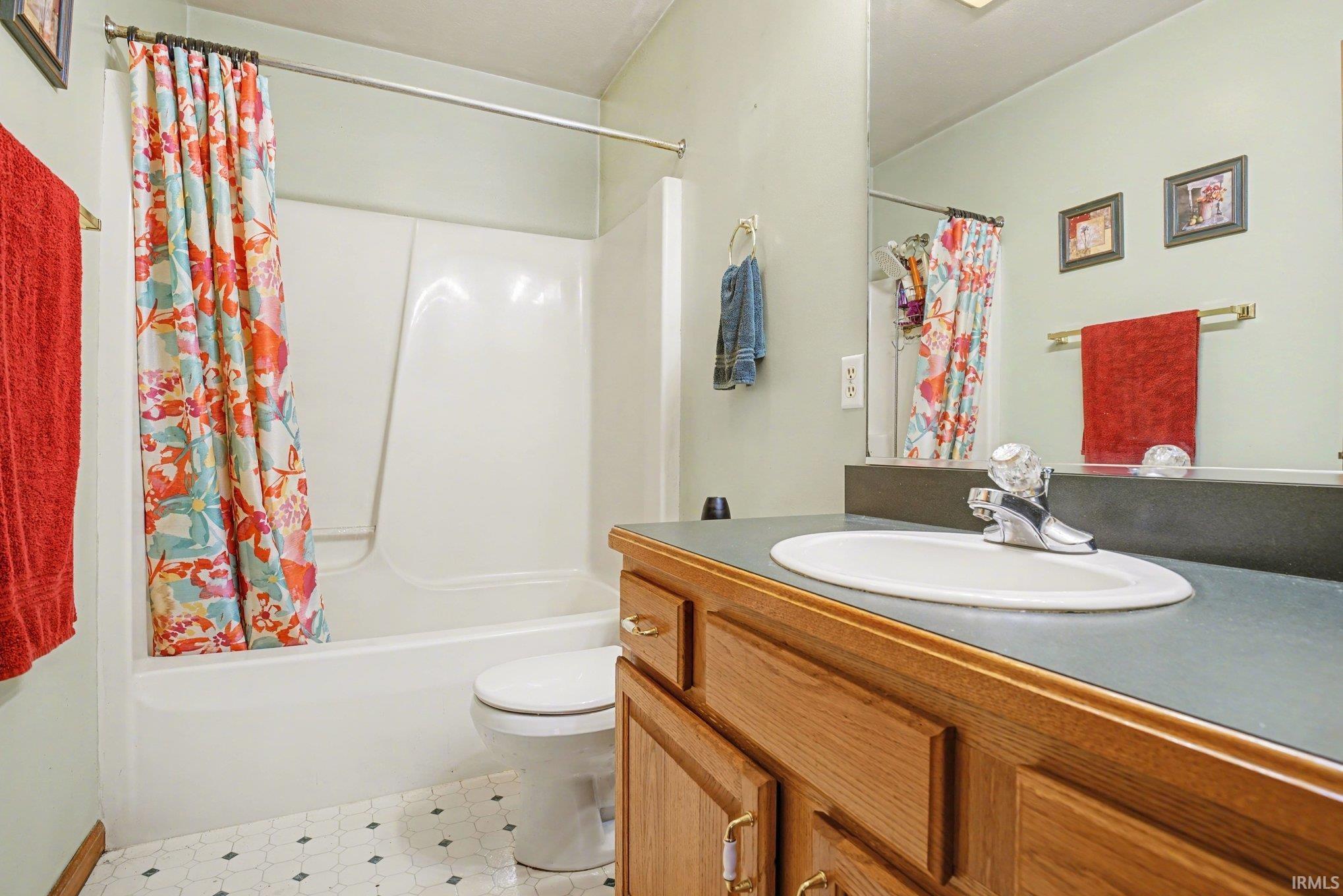 Bathroom featuring vanity, shower / bath combo with shower curtain, and light floors