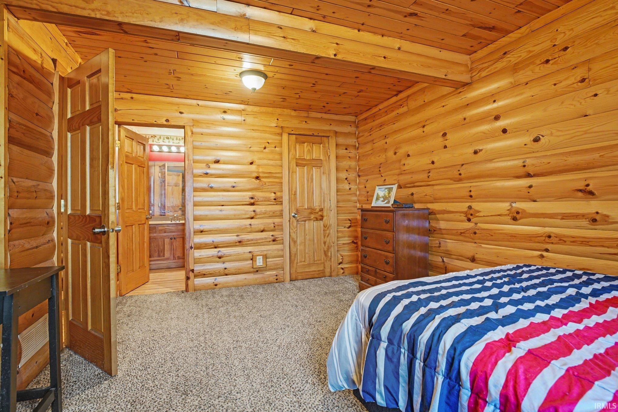 Carpeted bedroom with rustic walls, wooden ceiling, and ensuite bath